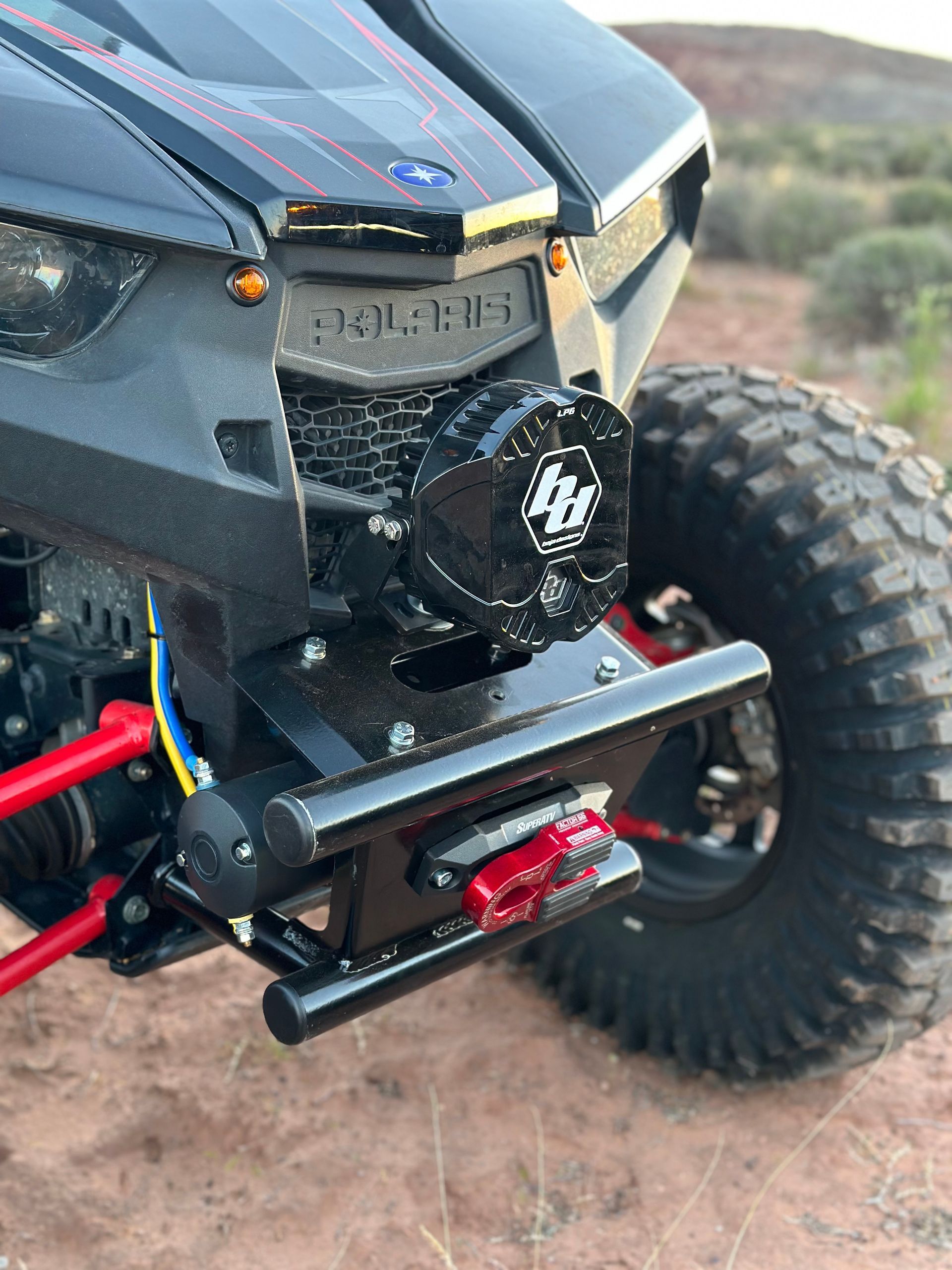 Close-up of a black RC off-road truck with red suspension and large treaded tires on dirt.