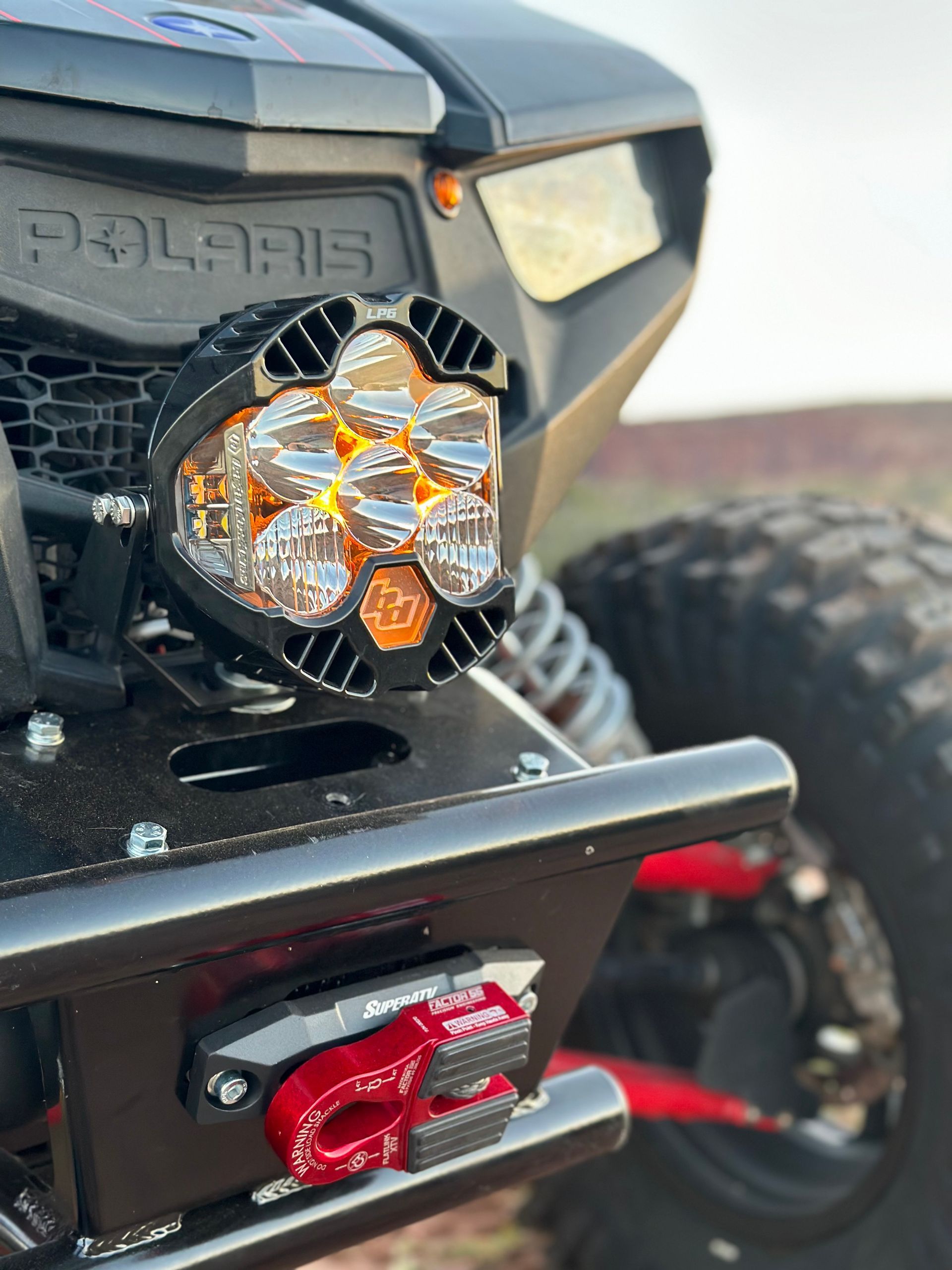 Front view of a Polaris off-road vehicle with a round LED light and red winch hook on the bumper