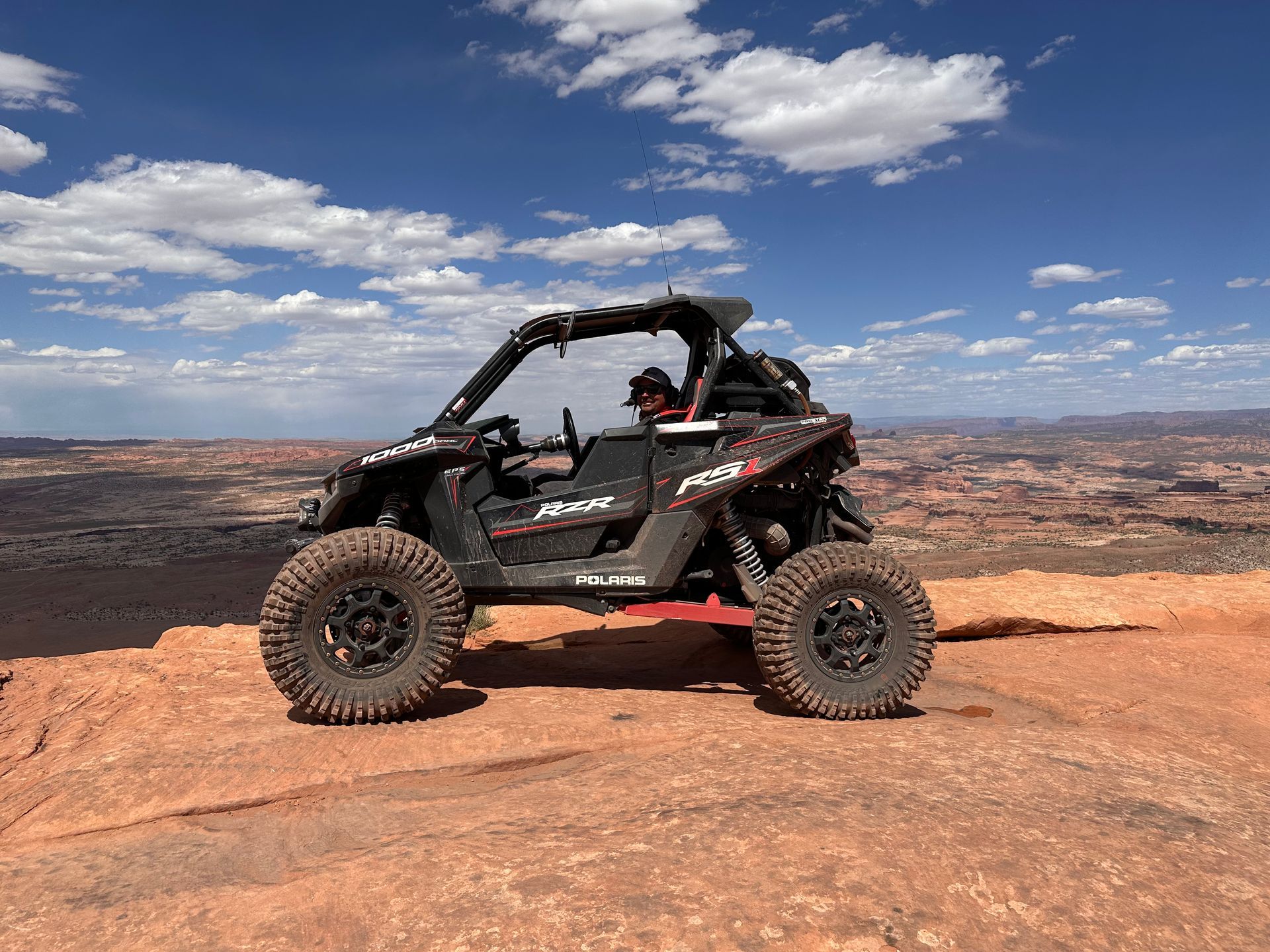 Off-road side-by-side on a rocky desert overlook under a blue sky with scattered clouds