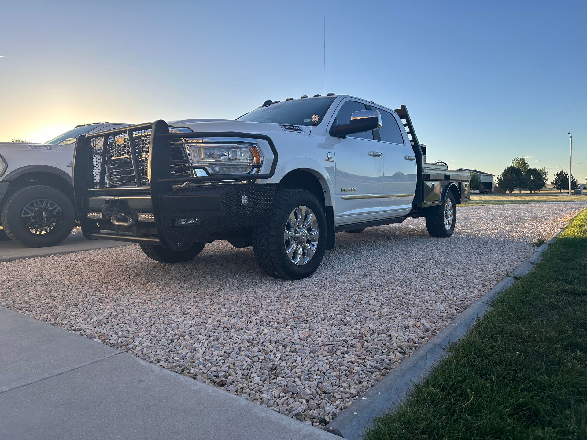 White pickup truck parked on gravel at sunset, with a grassy edge and clear blue sky.