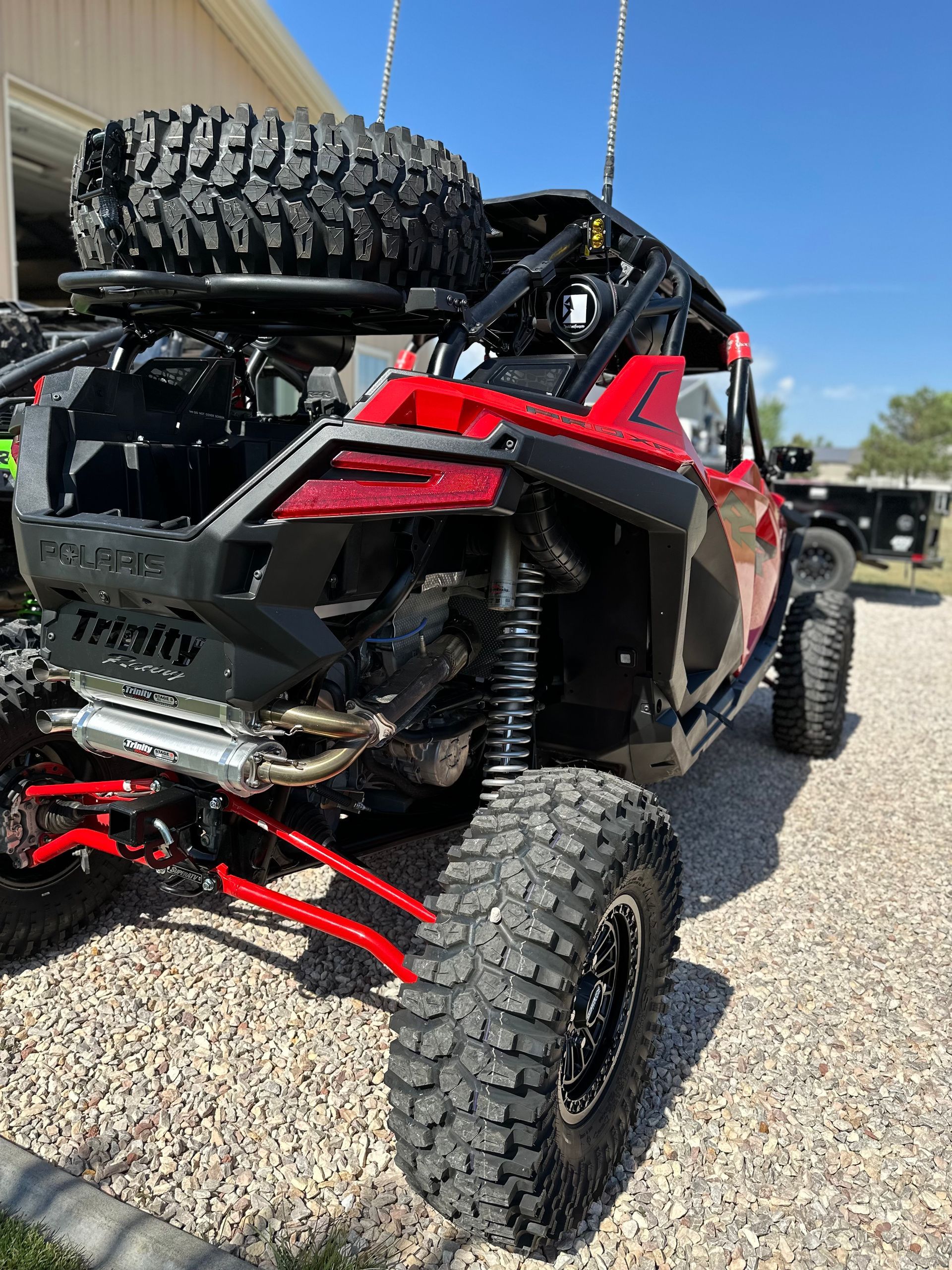Damaged red-and-black off-road vehicle parked on gravel, with a spare tire mounted on top.