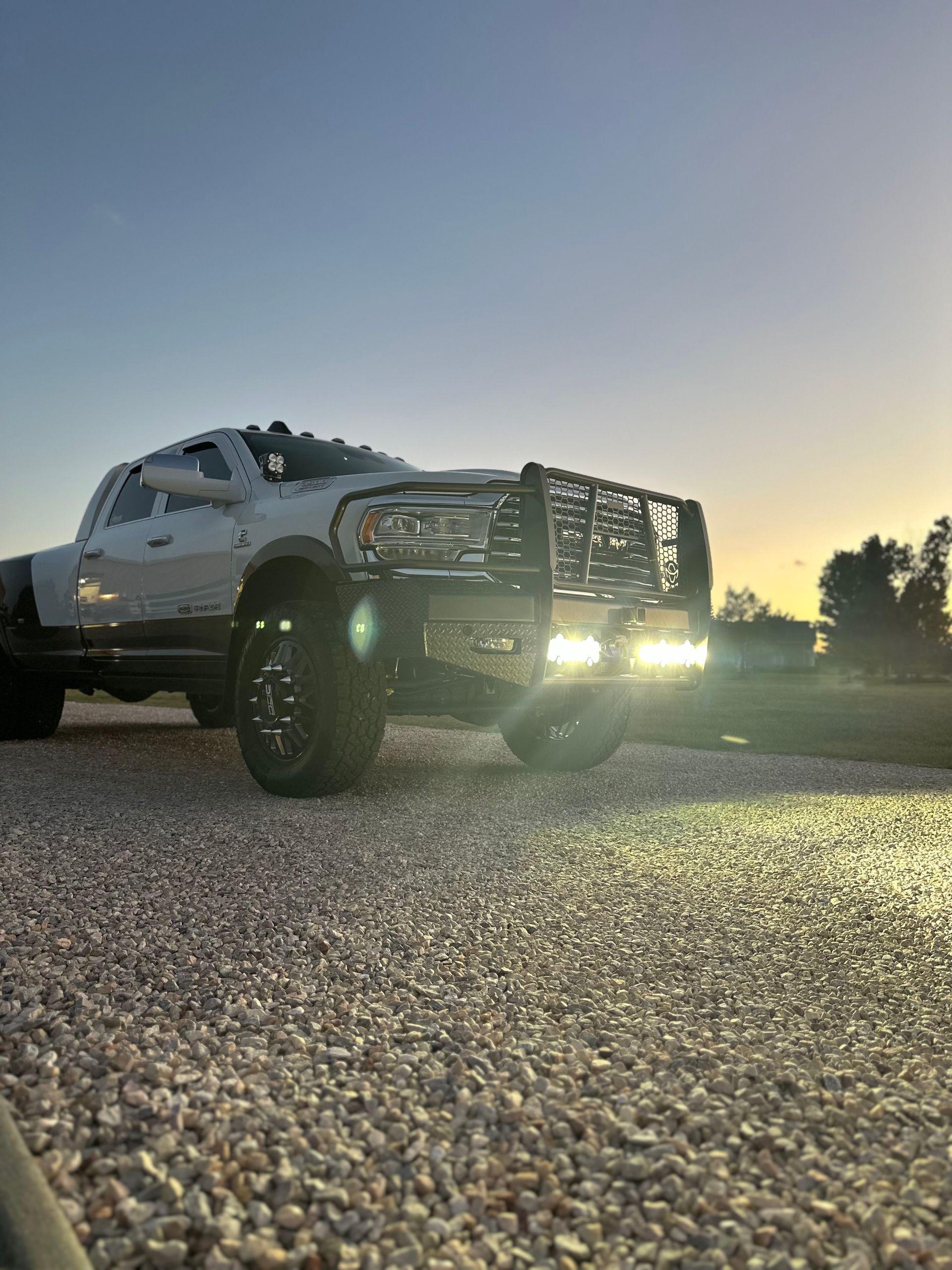 Lifted white pickup truck with bright headlights on a gravel road at dusk