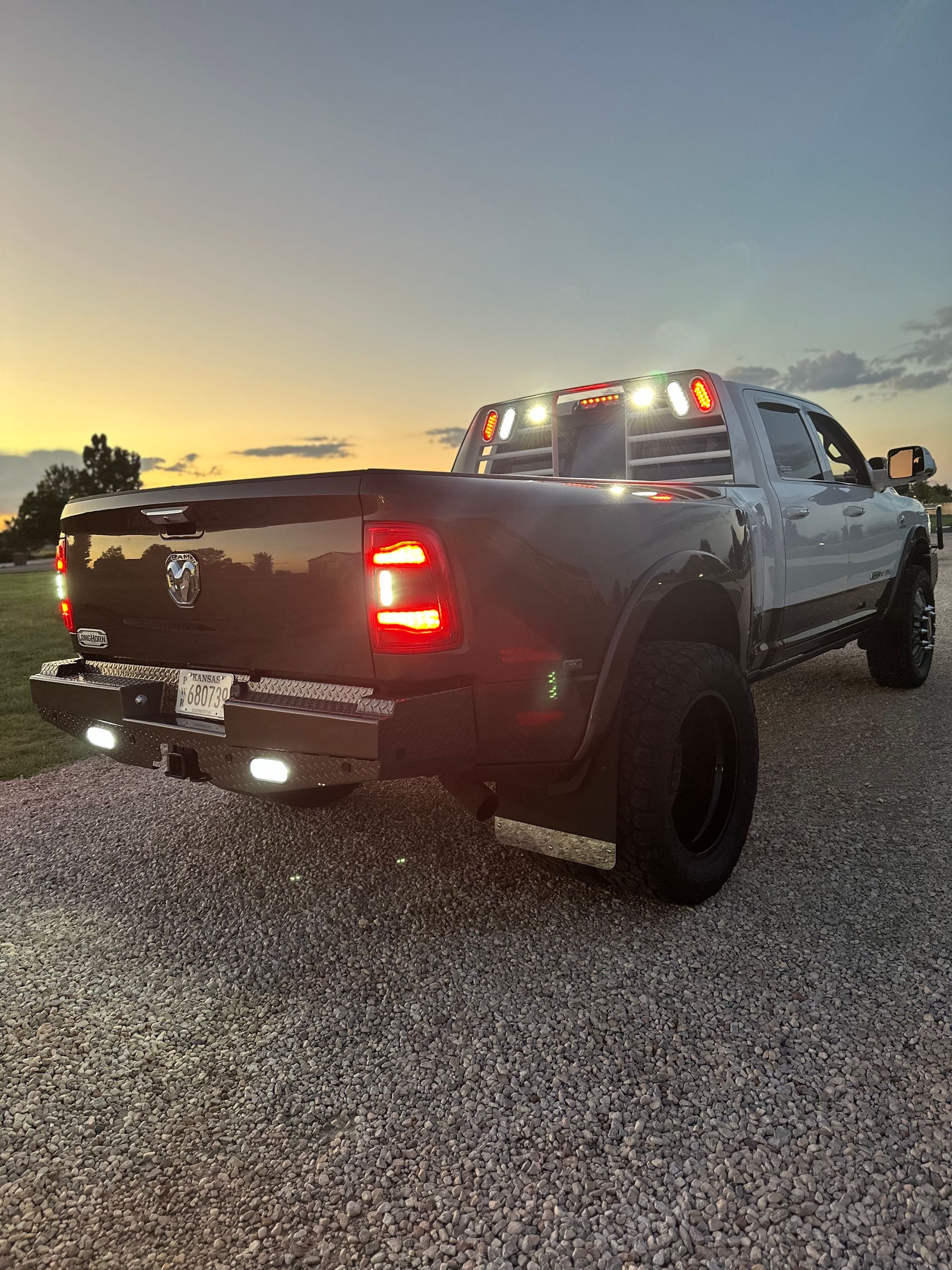 Black pickup truck at sunset on a gravel lot, rear lights on with roof marker lights lit.