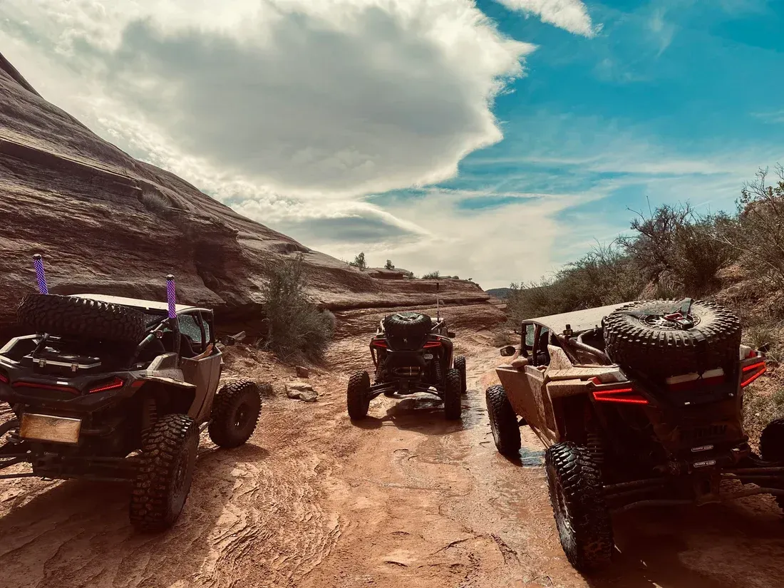Off-road vehicles driving on a muddy mountain trail under a cloudy sky