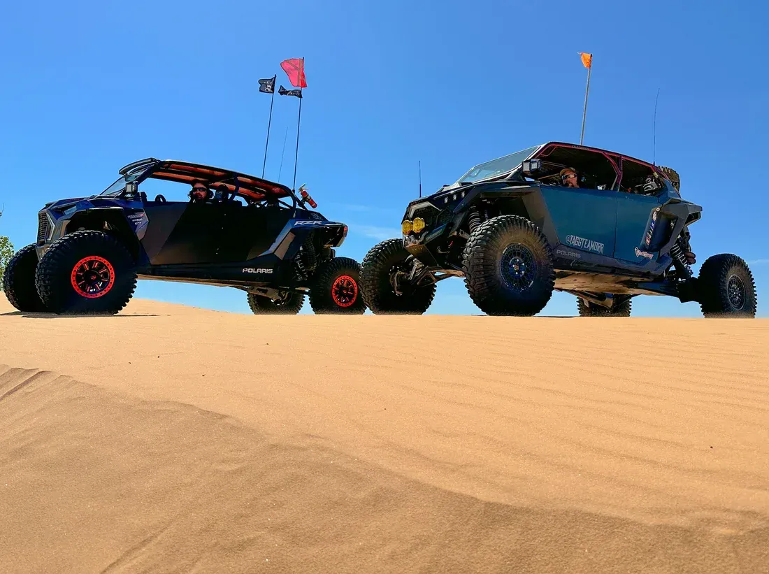 Two off-road dune buggies on sand dunes under a clear blue sky