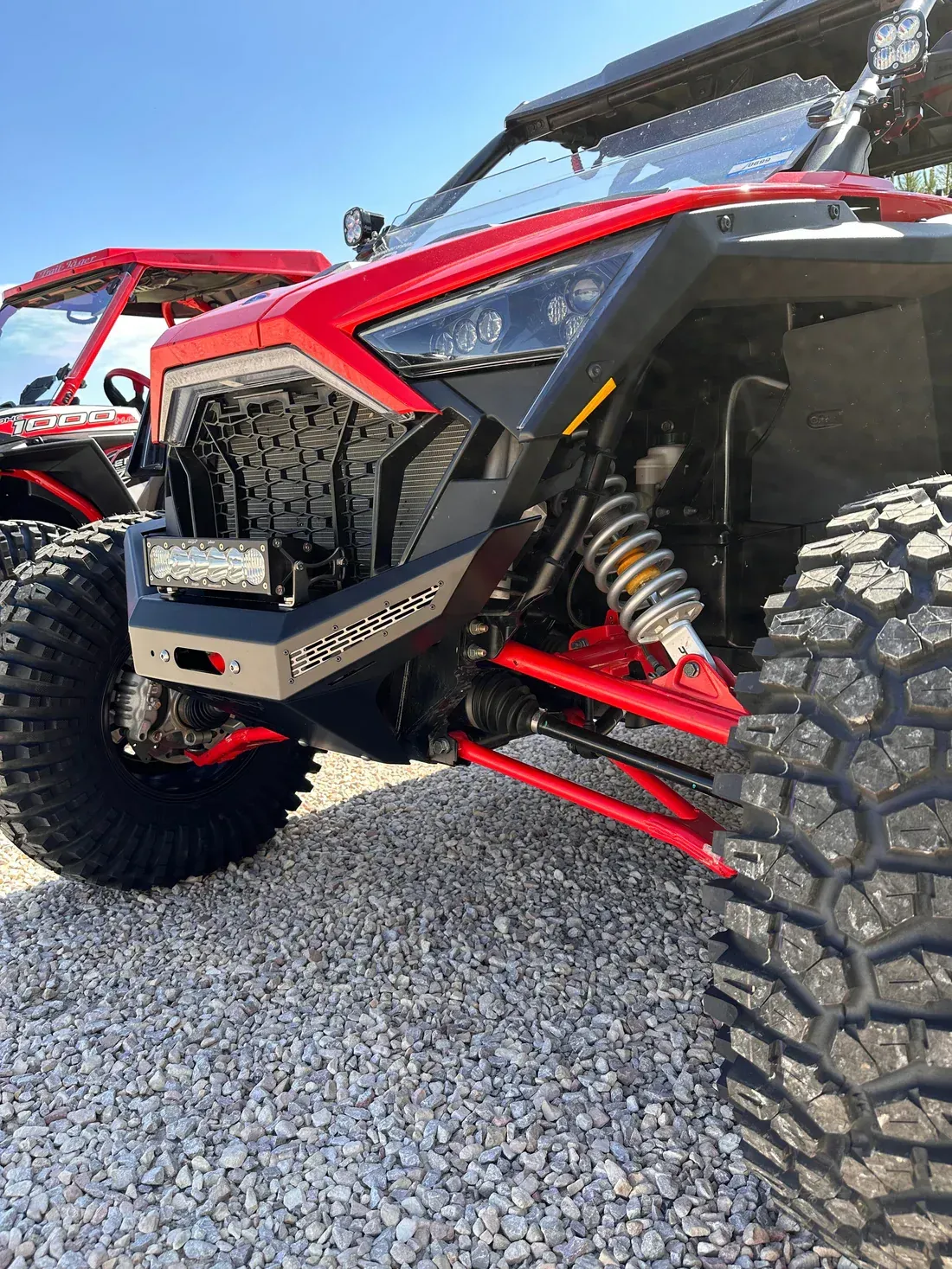 Red off-road side-by-side ATV with large knobby tires on gravel under a canopy