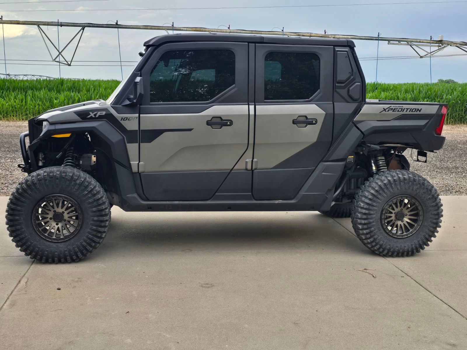 Black lifted four-door off-road truck parked on pavement with large tires and a rear-mounted gun rack