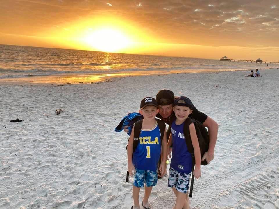 A man and two boys are standing on a beach at sunset.