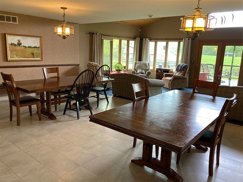 Dining area with two large wooden tables, chairs, and a seating area with a sofa, and large windows.