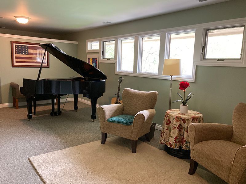 A black grand piano in a room with two armchairs, a table, and a rug.
