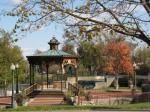 Gazebo in a park, surrounded by trees. Red brick path and steps. Autumn foliage.