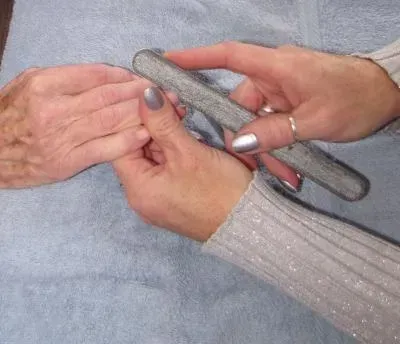 Hands filing a fingernail on another hand, light blue cloth background.
