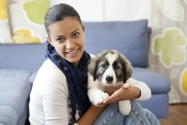 Woman holding a puppy on her lap; both smiling in a living room.