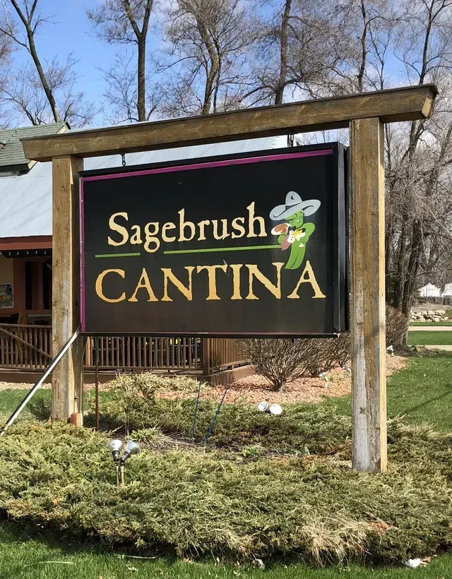 Sign for Sagebrush Cantina restaurant: black background, gold text, cartoon chili pepper wearing a sombrero.