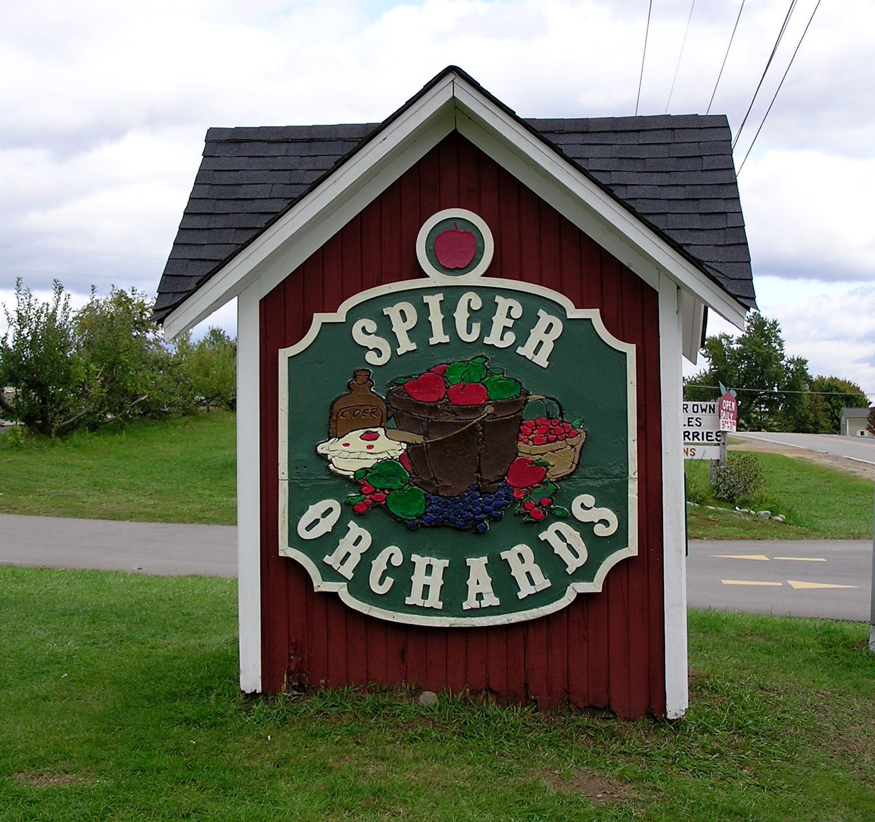 Sign for Spicer Orchards, with green and white text on a red and green background, set in a wood structure.