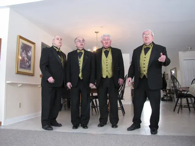 Four men in black suits and gold vests standing indoors. One man gives a thumbs up.