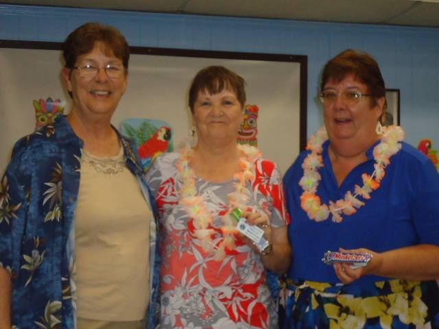 Three women are posing for a picture and one is wearing a lei