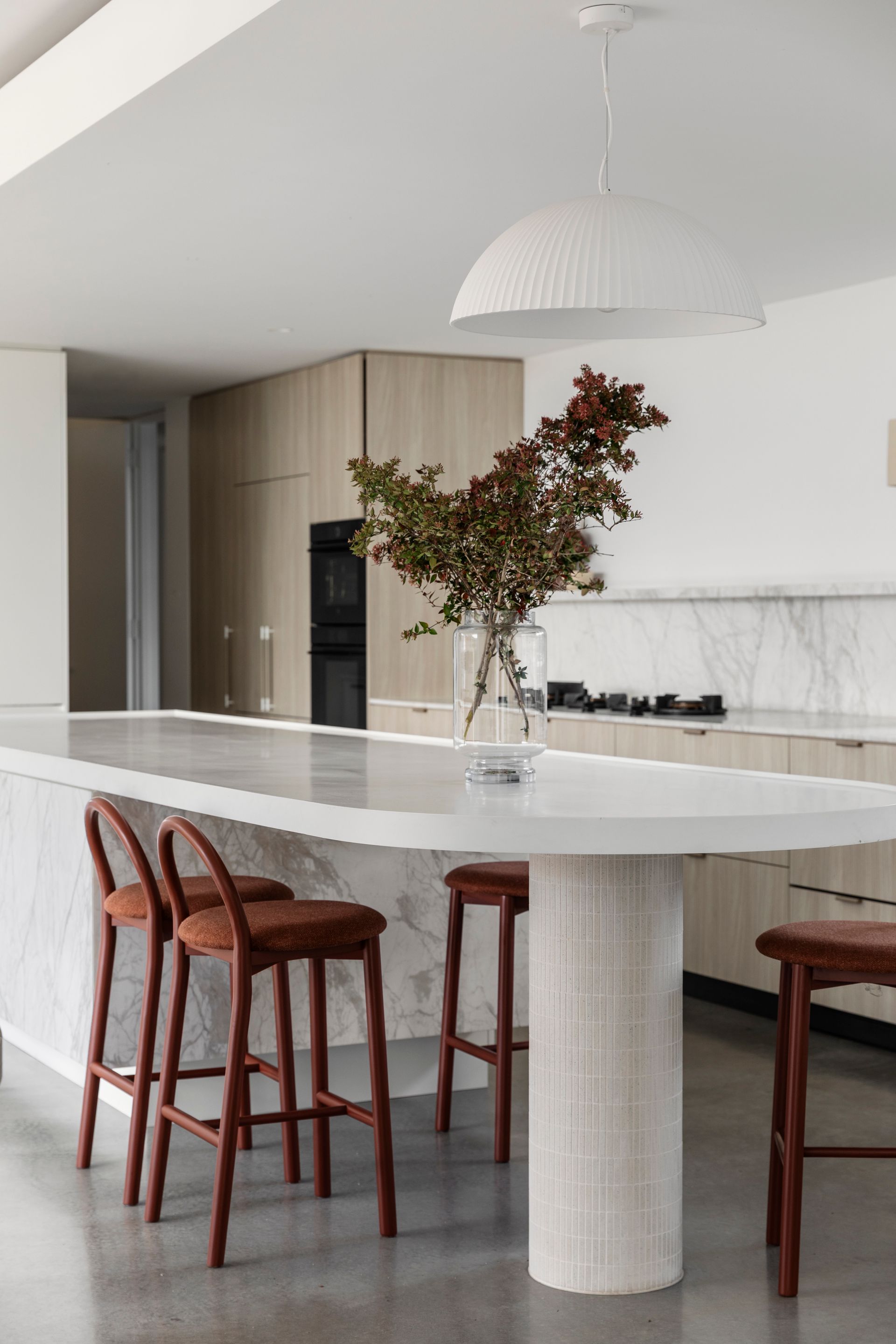 Modern kitchen with long island and bar stools, light wood cabinets, and large dome light fixture — Escarpment Building in Austinmer, NSW