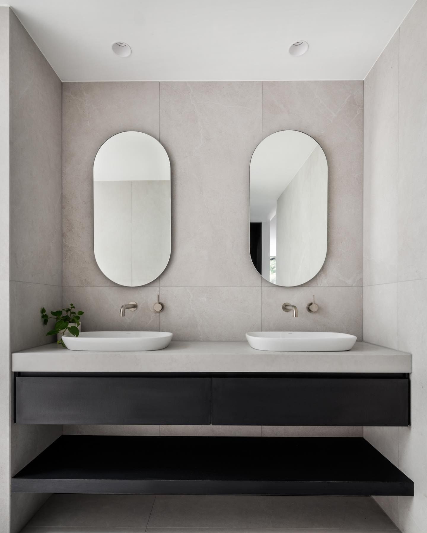 Modern bathroom with two oval mirrors, gray tile, and a black floating vanity — Escarpment Building in Austinmer, NSW
