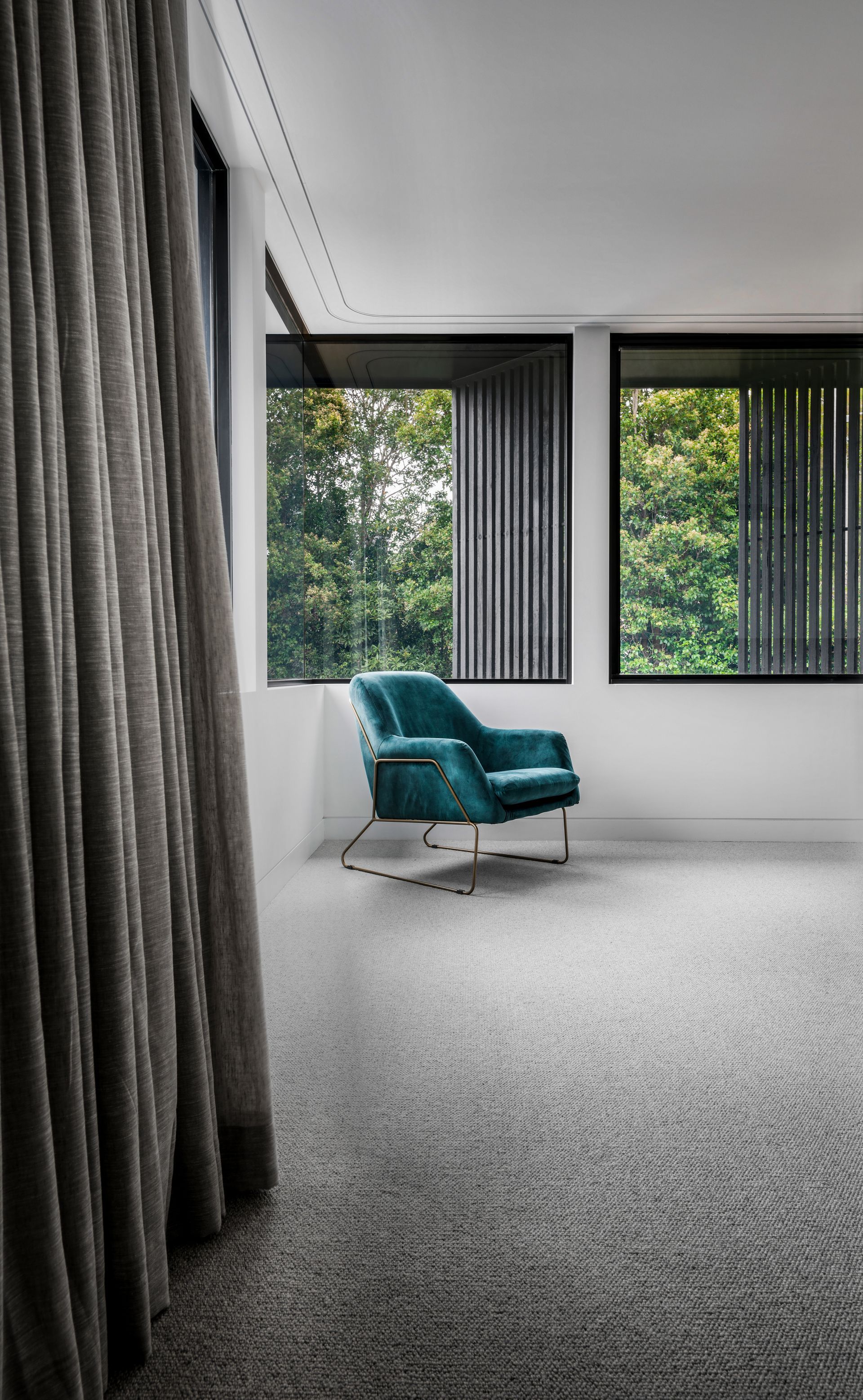 Teal velvet armchair in a modern room with large windows, gray carpet, and sheer curtains — Escarpment Building in Austinmer, NSW