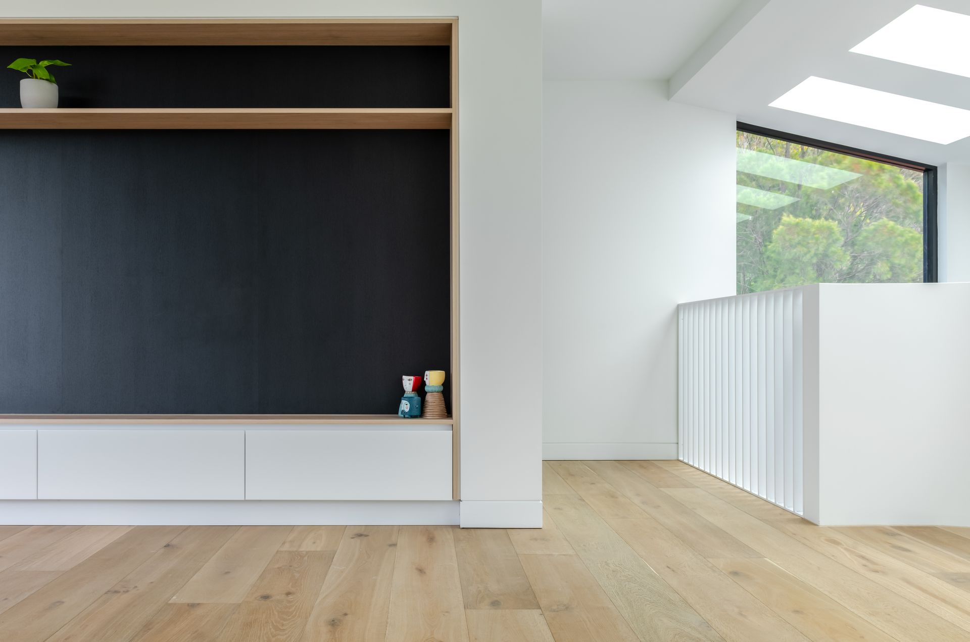Modern interior with wood floors, built-in black wall unit, white railing, and skylight — Escarpment Building in Austinmer, NSW