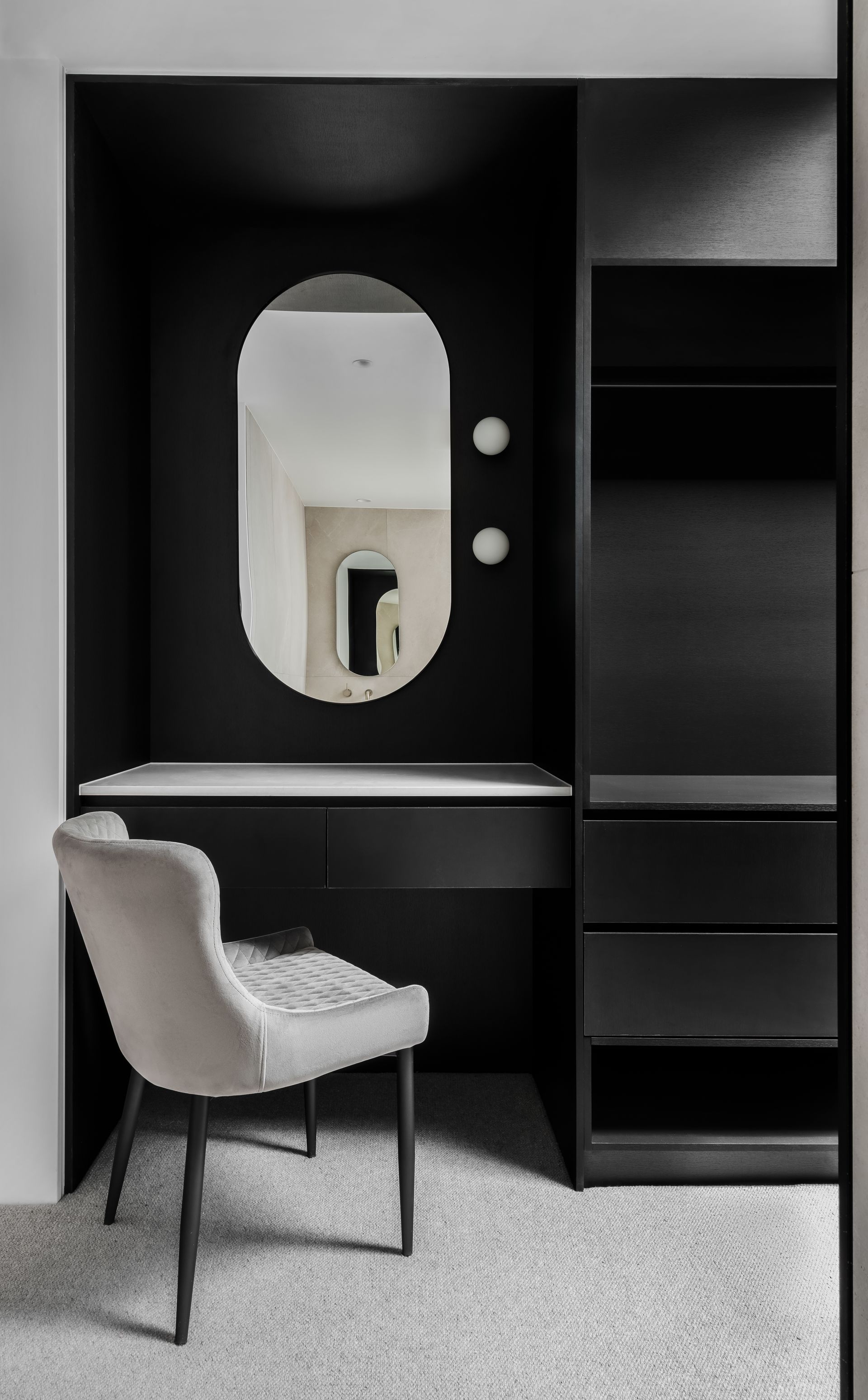 Black vanity nook with oval mirror, shelves, desk, and grey upholstered chair — Escarpment Building in Austinmer, NSW