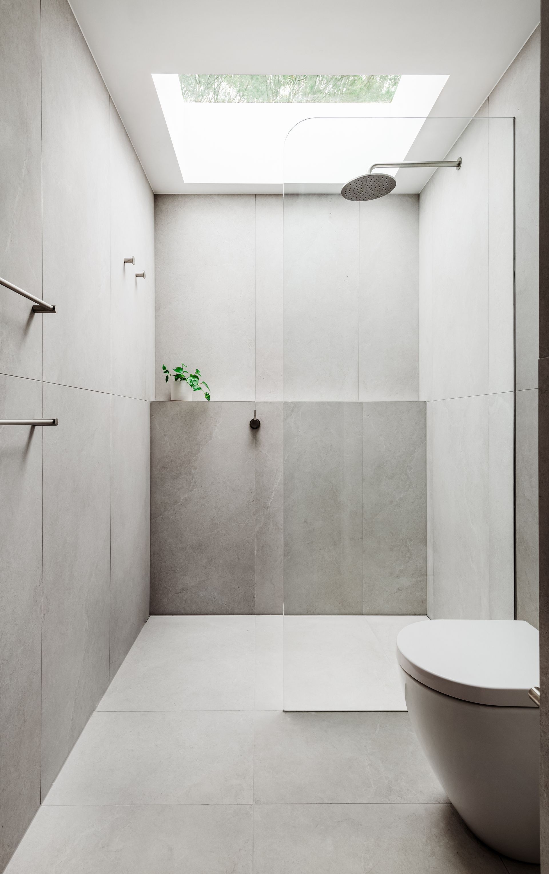Minimalist white bathroom with showerhead, toilet, and skylight — Escarpment Building in Austinmer, NSW