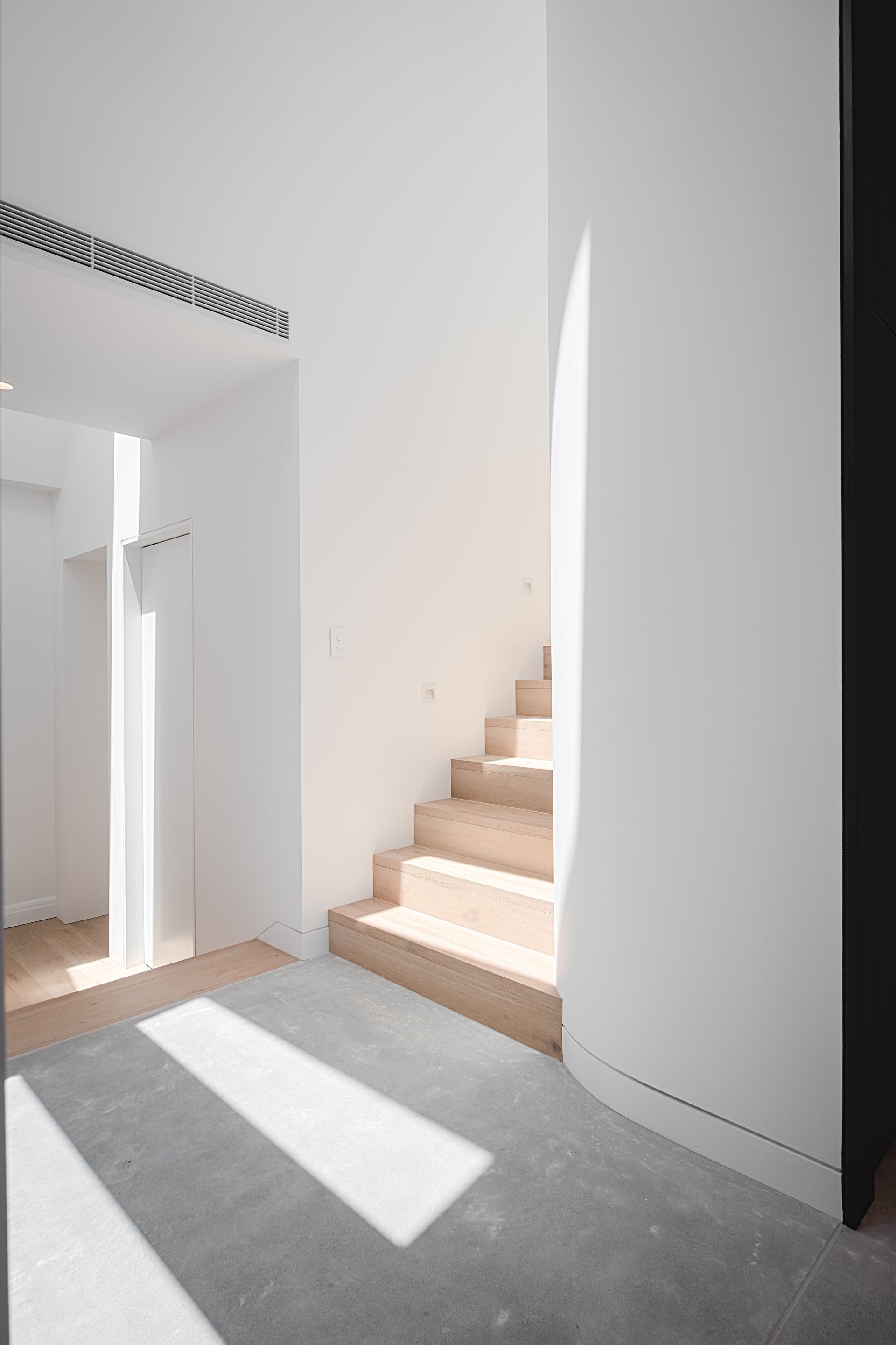 Bright interior with staircase and light streaming down. White walls, wooden stairs, and grey carpet — Escarpment Building in Austinmer, NSW