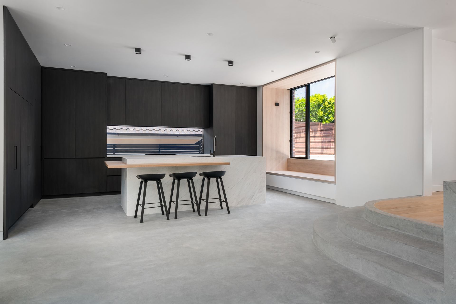 Modern kitchen with dark cabinetry, white island with stools, and large window — Escarpment Building in Austinmer, NSW