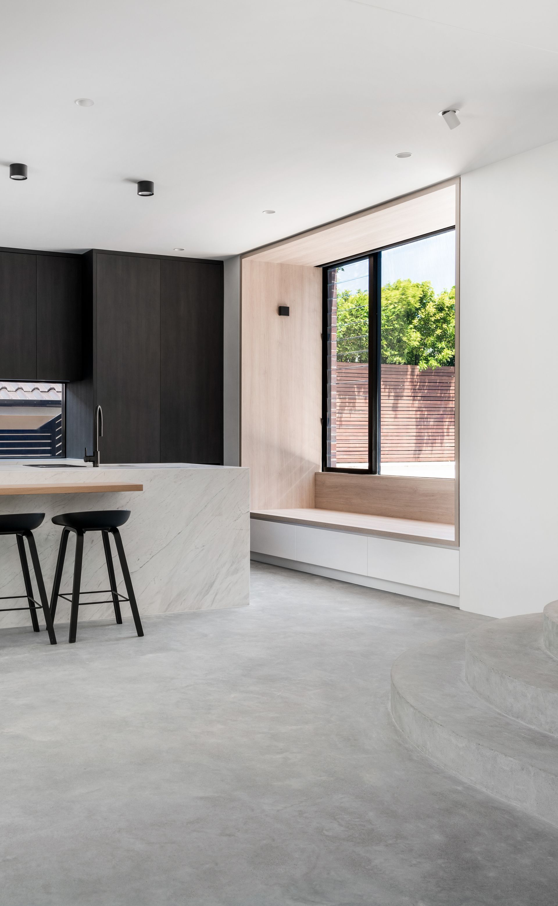 Modern kitchen interior with dark cabinetry, light countertops, and a large window with a built-in bench — Escarpment Building in Austinmer, NSW