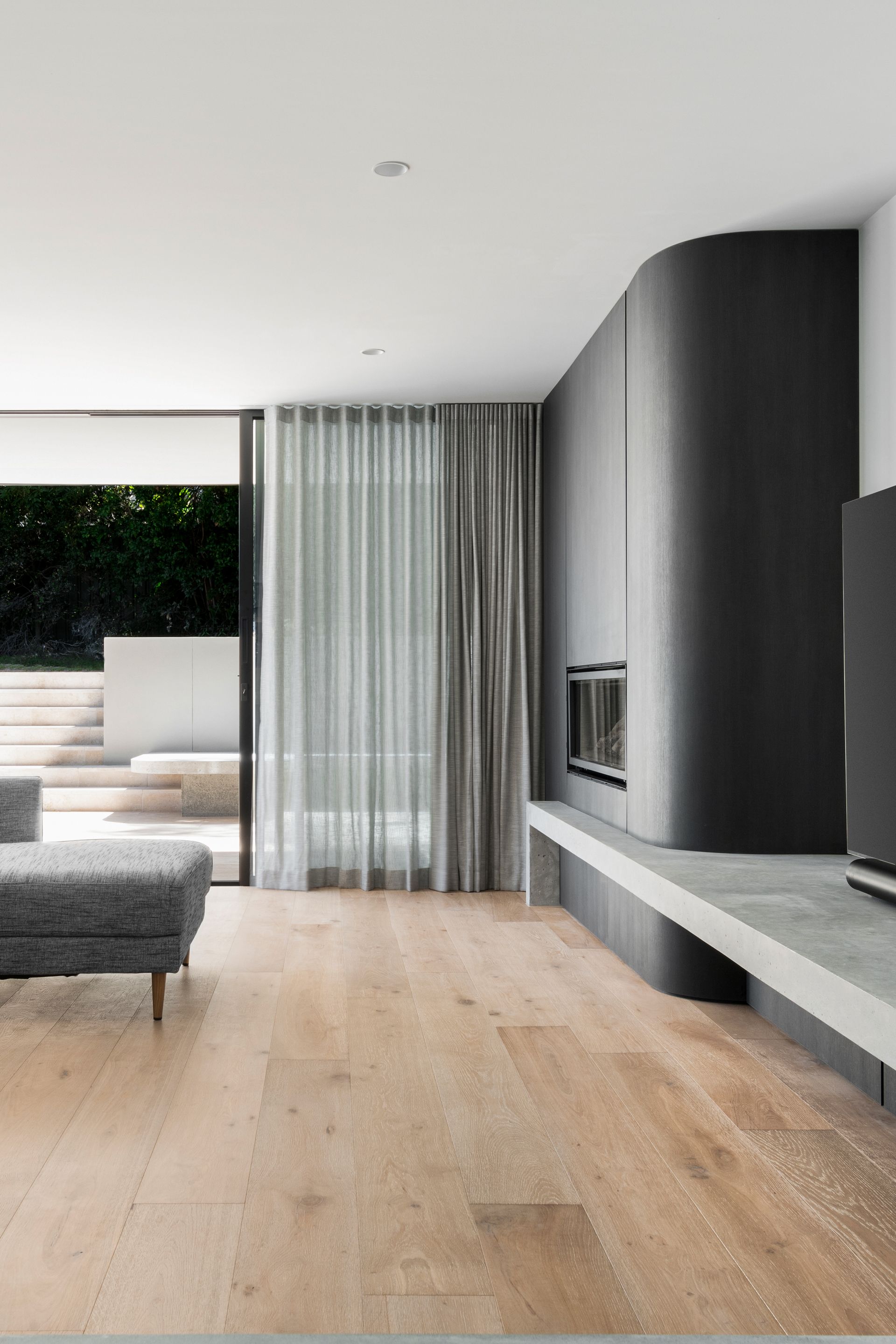 Modern living room with a gray fireplace, sheer curtains, and light wooden floors — Escarpment Building in Austinmer, NSW