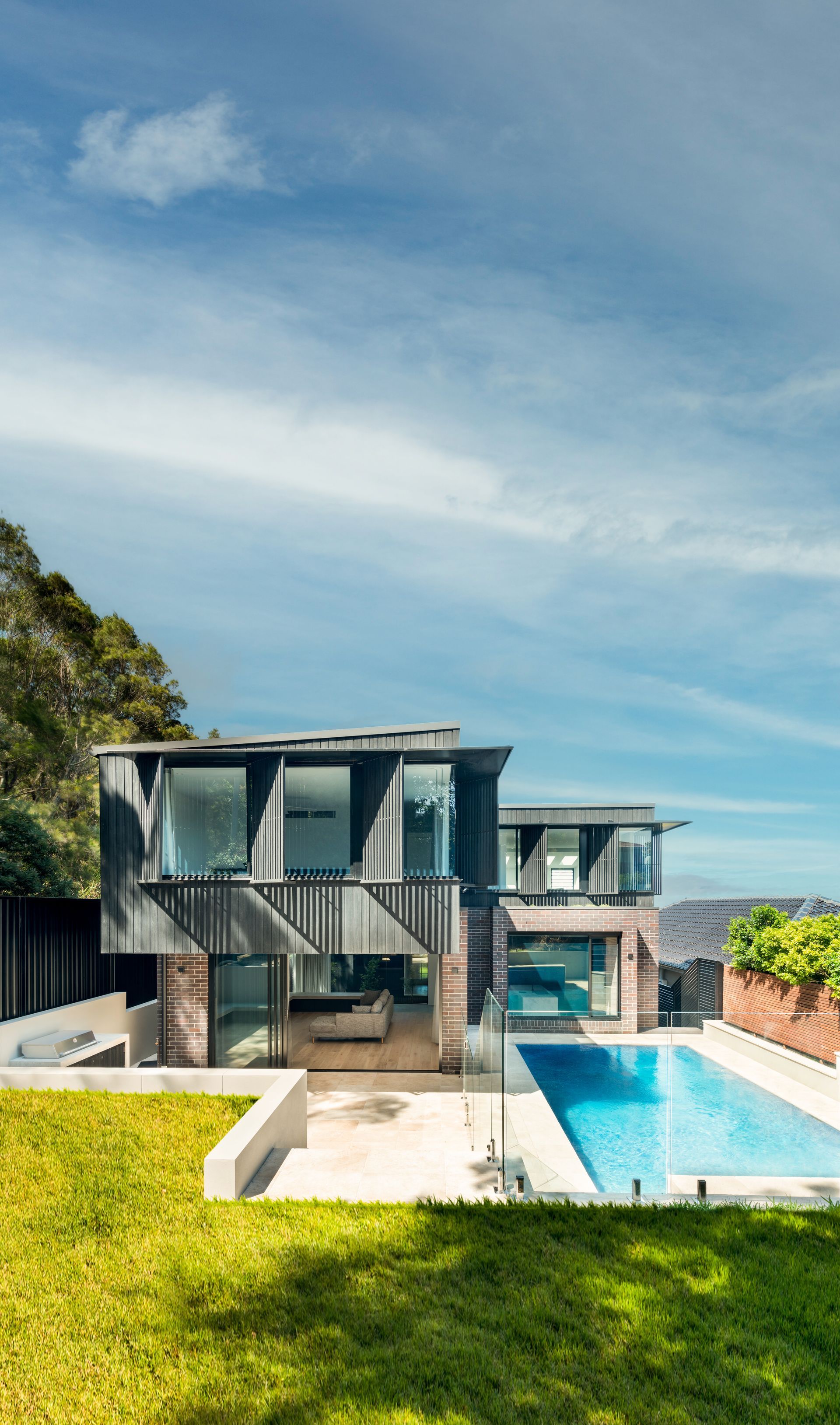 Modern house with pool, tall glass windows, and green lawn under a partly cloudy blue sky — Escarpment Building in Austinmer, NSW
