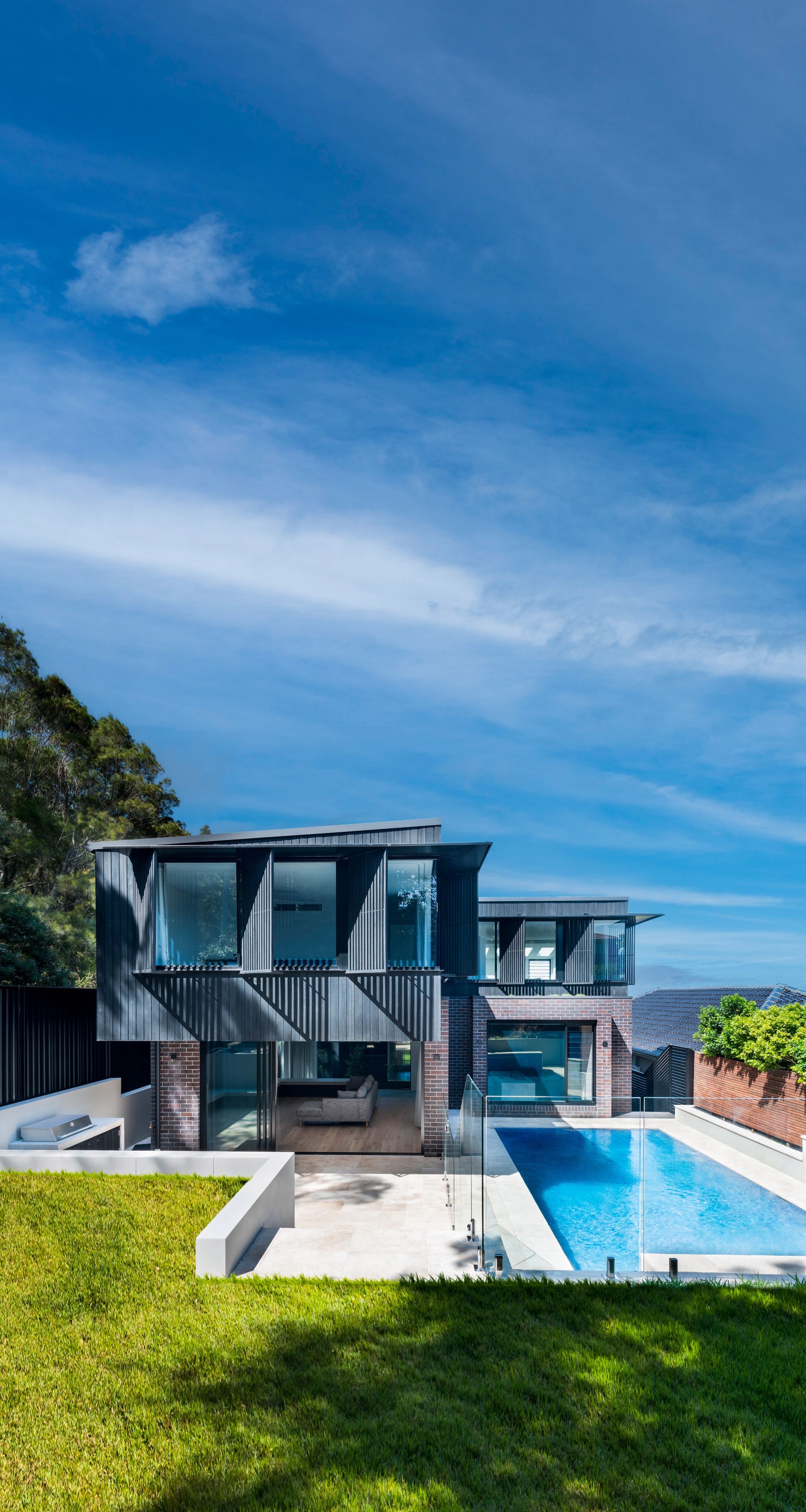 Modern home with a pool, blue sky. Grey exterior, green lawn — Escarpment Building in Austinmer, NSW