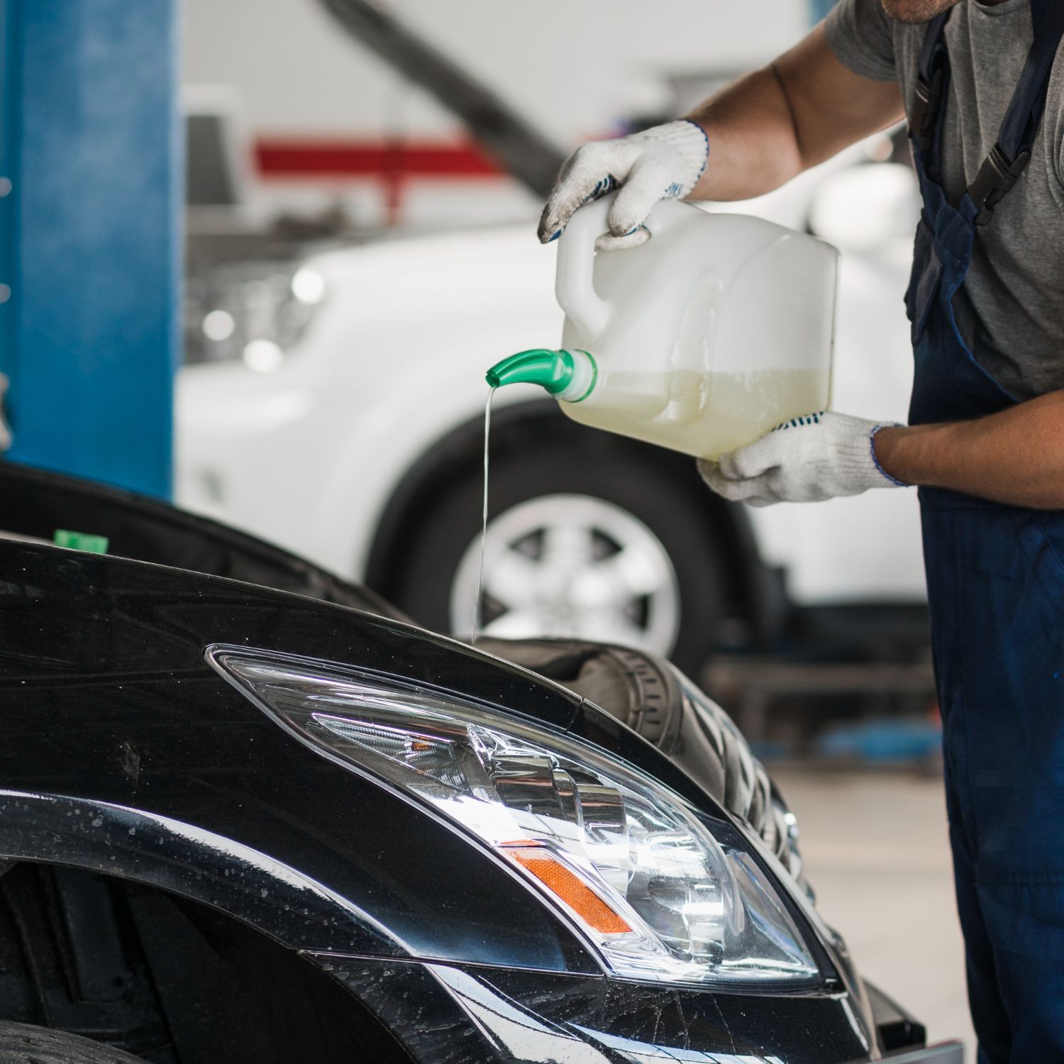 Mechanic pouring oil into a black car’s engine in a garage