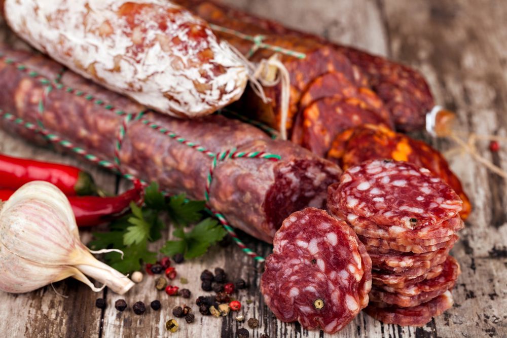 Embutidos variados, en lonchas y enteros, con ajos, pimientos y pimienta en grano sobre leña.