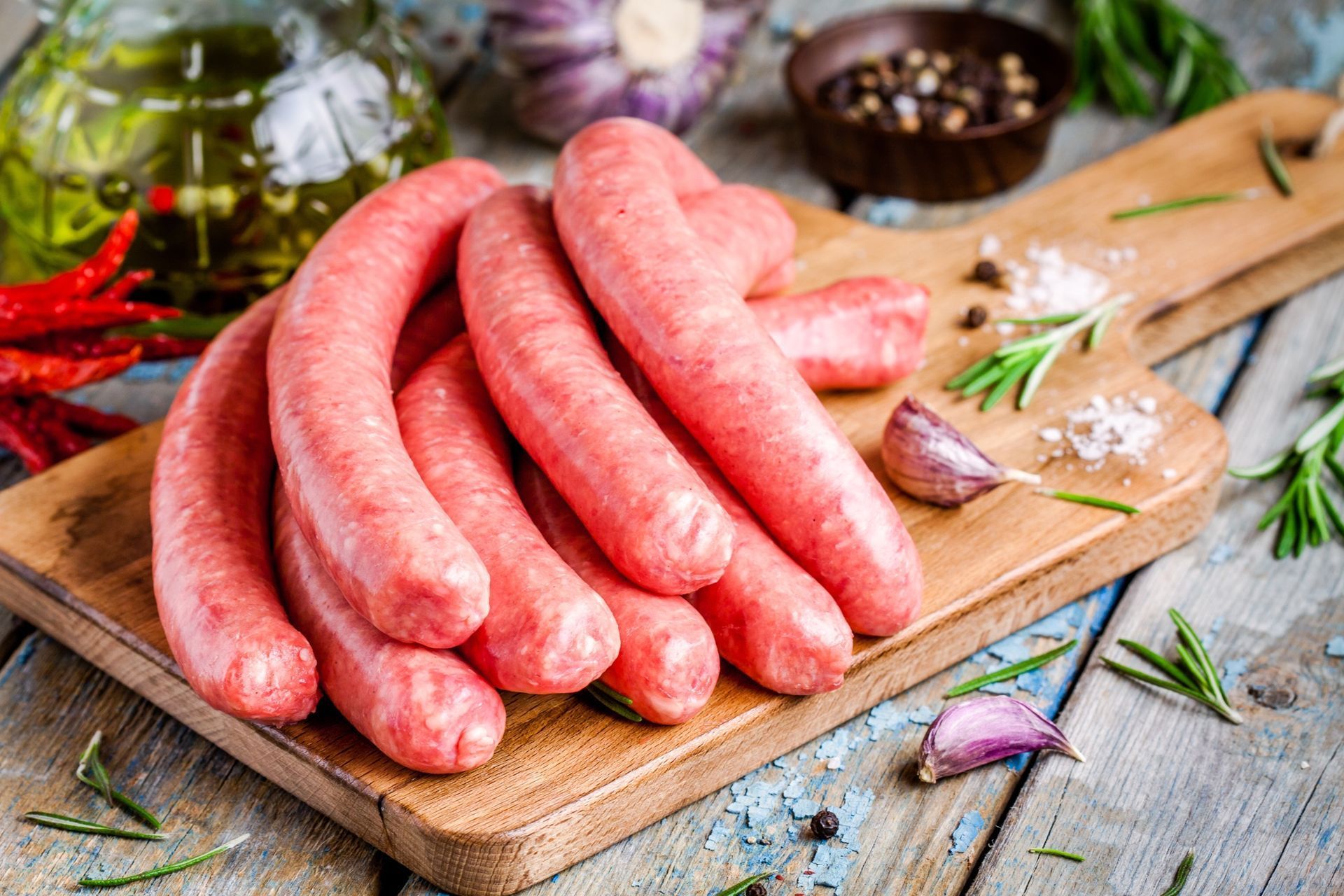 Salchichas crudas en una tabla de cortar de madera con ajo, hierbas y especias.