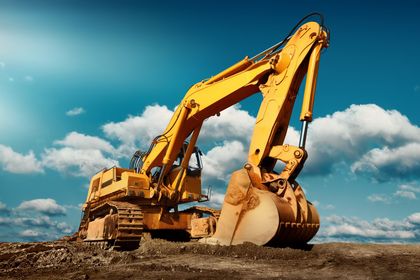 Yellow excavator at a construction site under a blue sky, digging into a dirt mound.