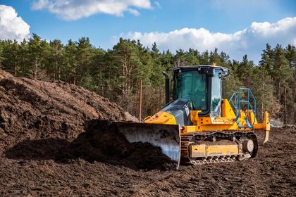 Yellow bulldozer pushing dirt at a construction site with trees in the background