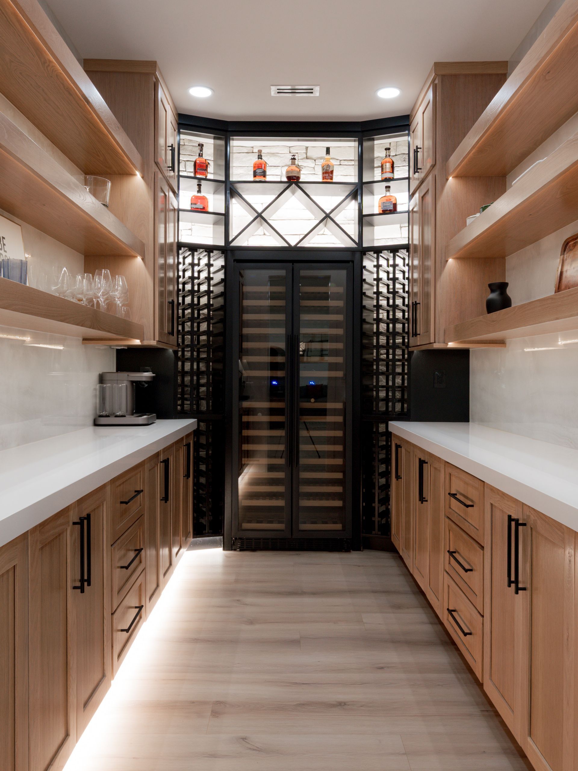 Narrow wine cellar with wooden shelves, cabinets, and a glass-door fridge at the end.
