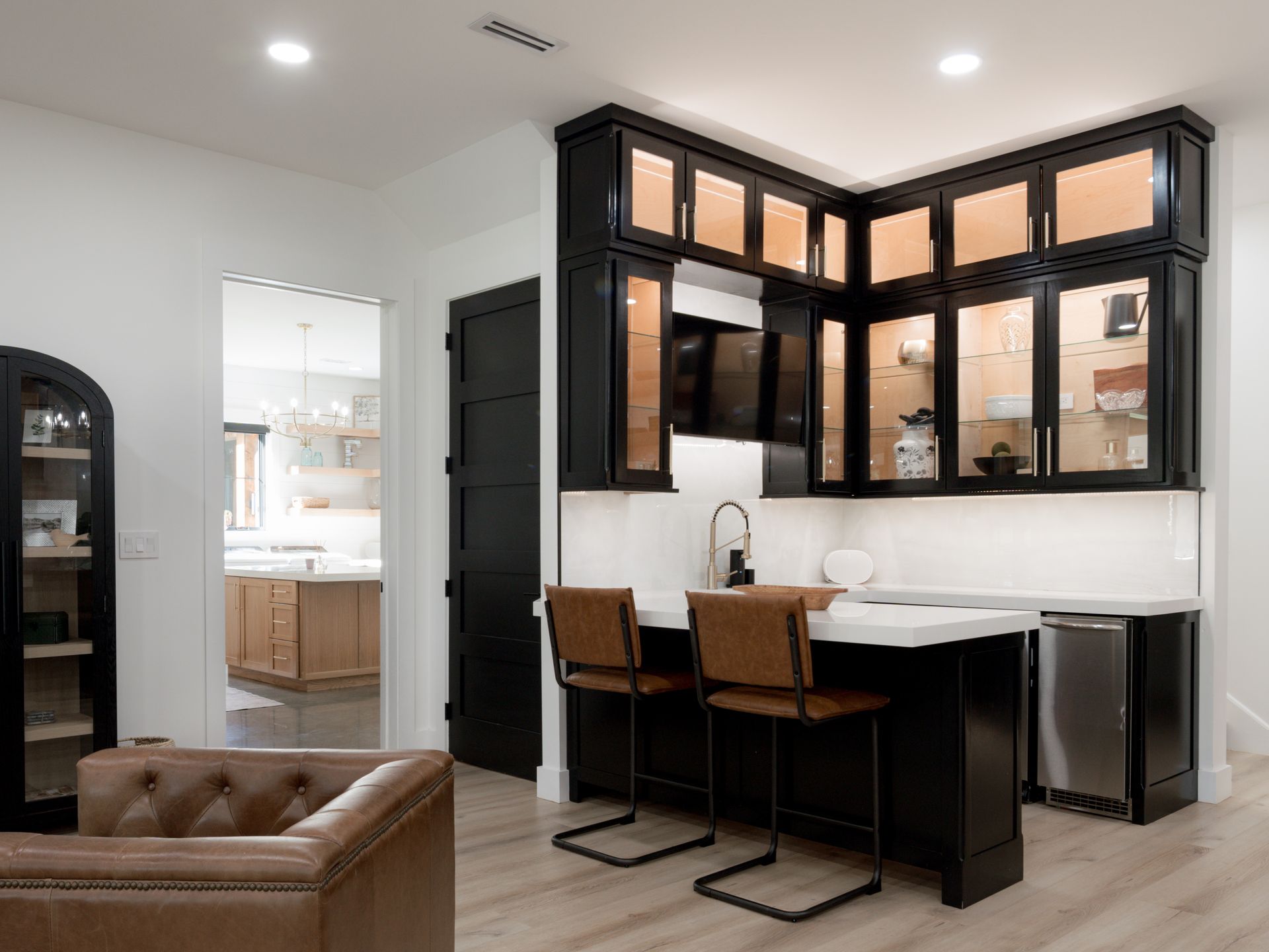 Modern open kitchen with black cabinets, white countertops, and two wooden bar stools.