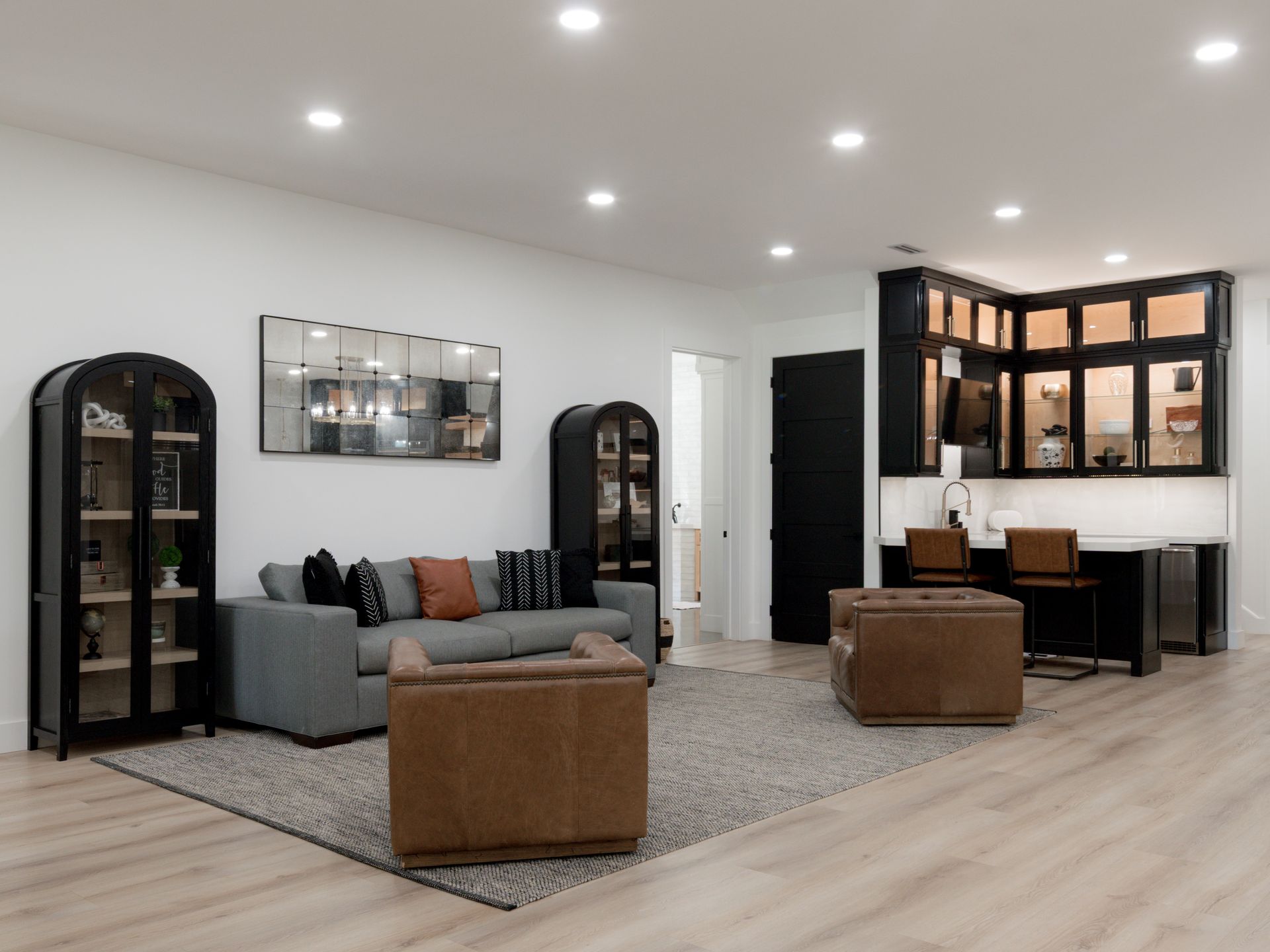 Modern living room with gray sofa, leather ottoman, arched cabinets, and black desk against white walls.