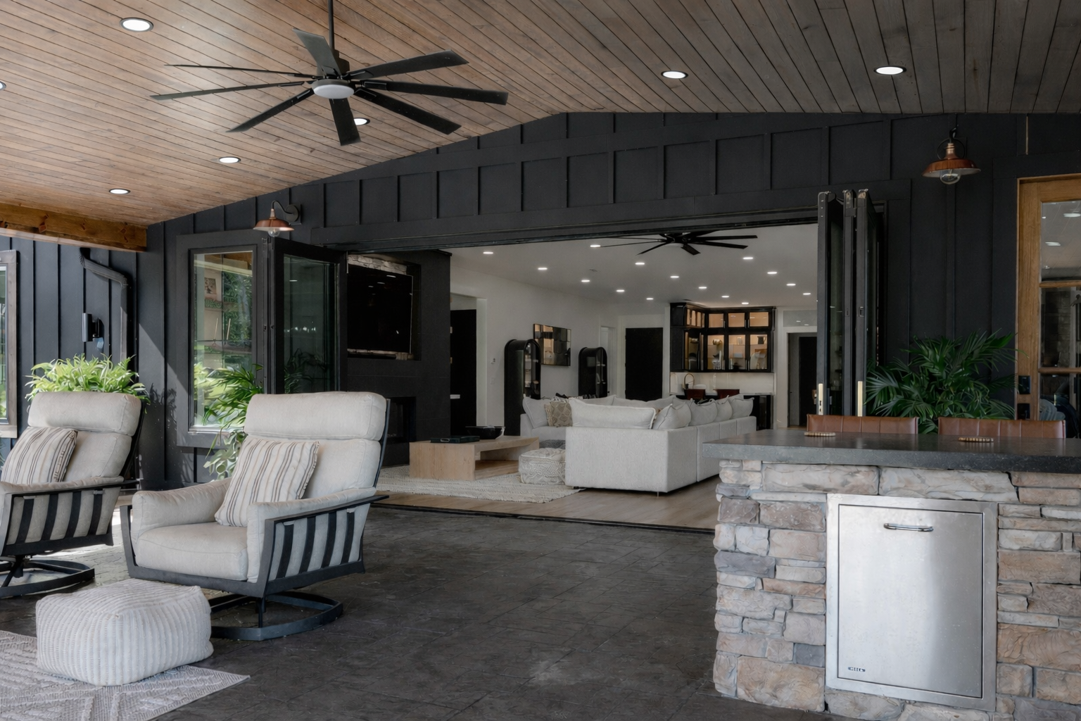 Covered patio with cushioned chairs, fire pit, ceiling fan, and an open view into a modern living room
