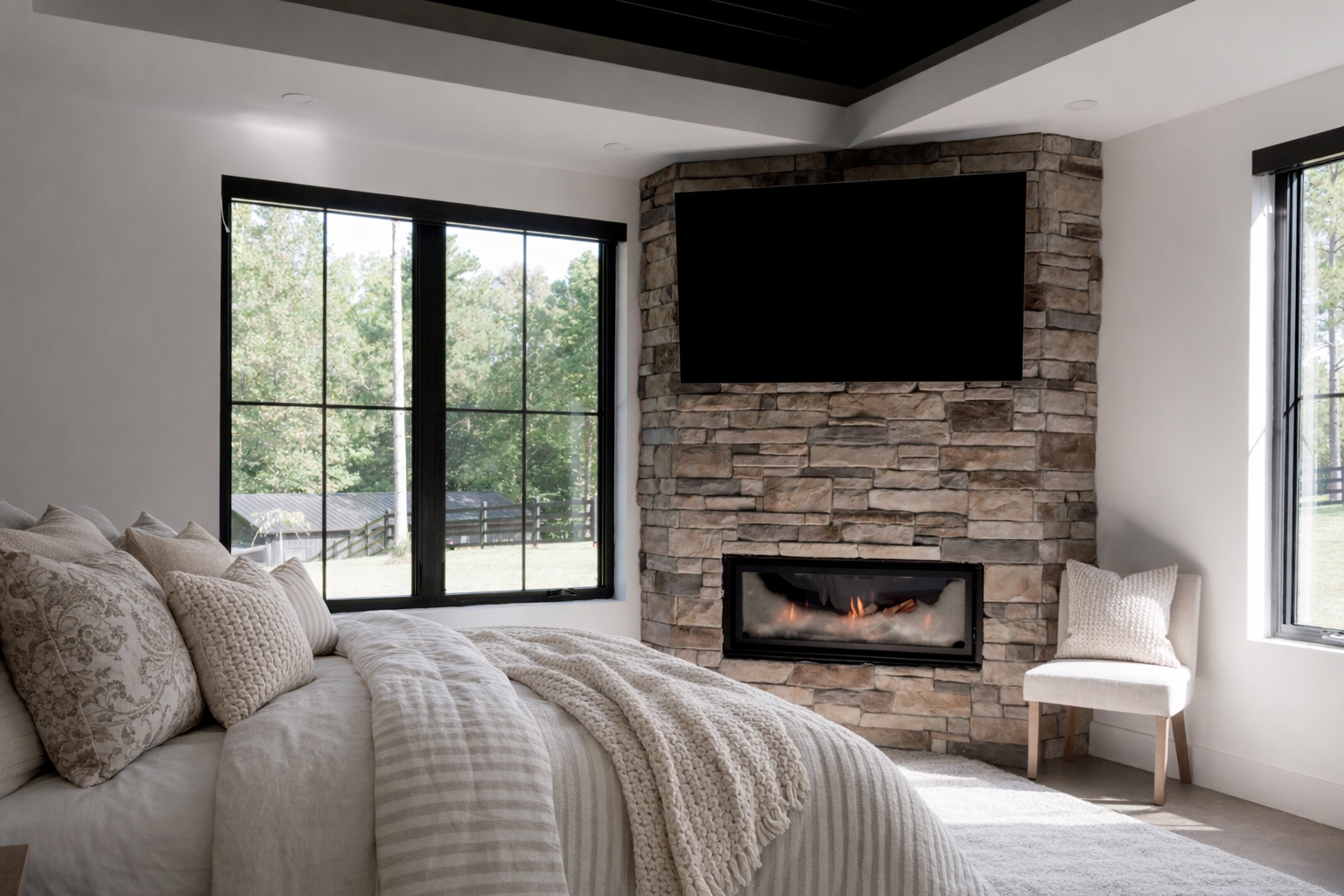 Modern bedroom with stone fireplace, wall-mounted TV, large windows, and a bed with neutral bedding