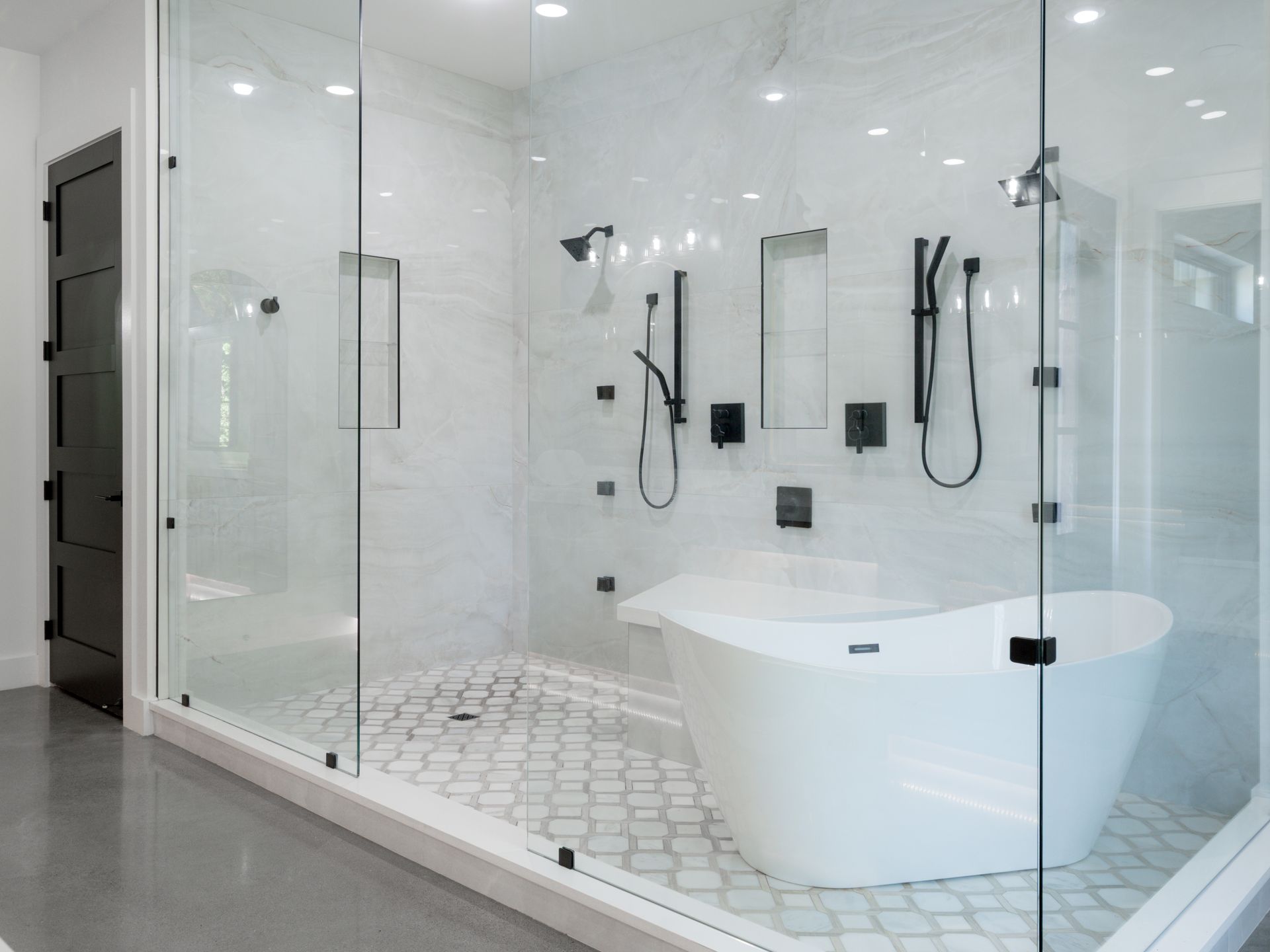 Modern white bathroom with glass shower, freestanding tub, and hex tile floor