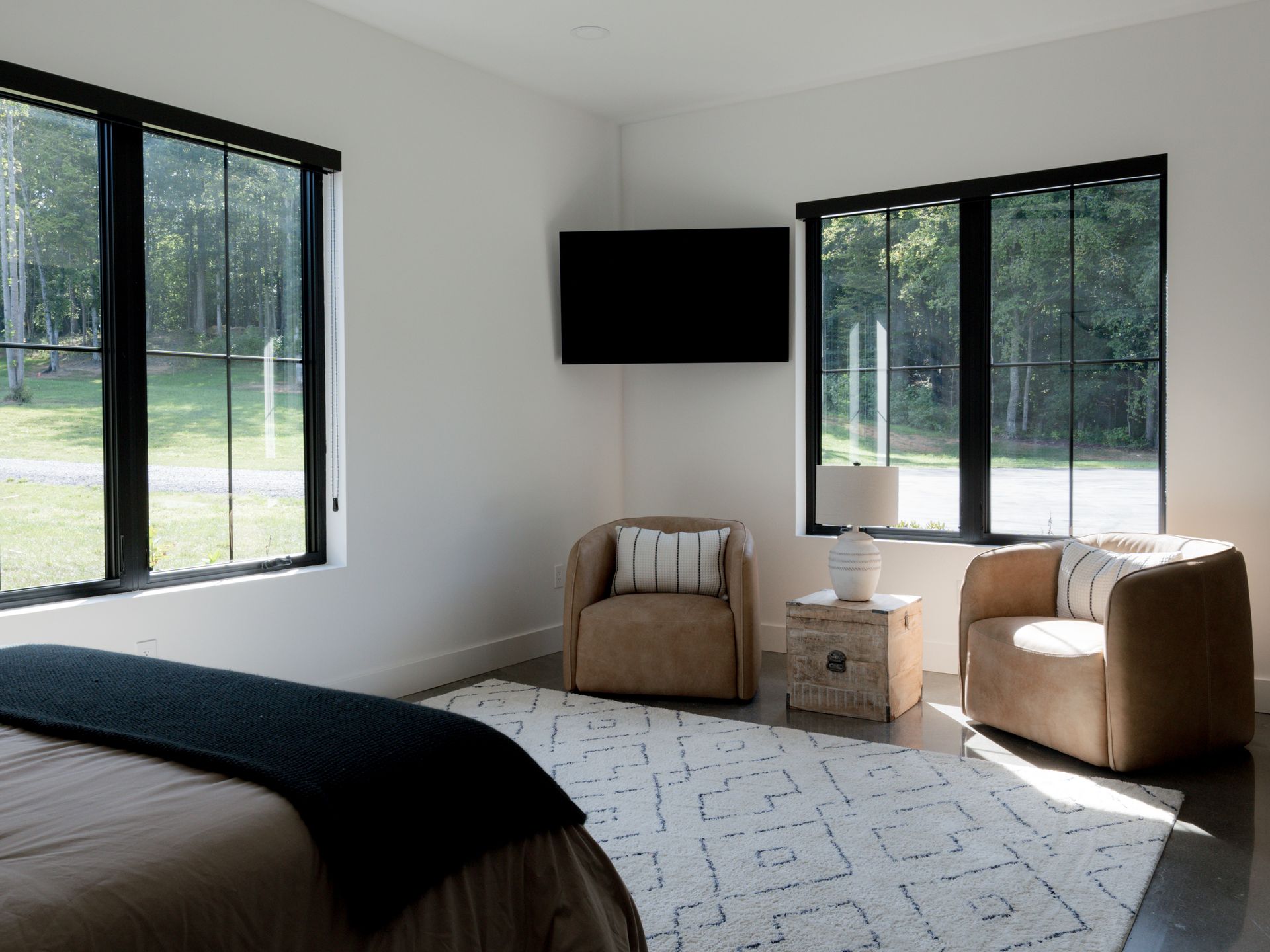 Modern bedroom with black-framed windows, wall-mounted TV, and two beige chairs by a small table