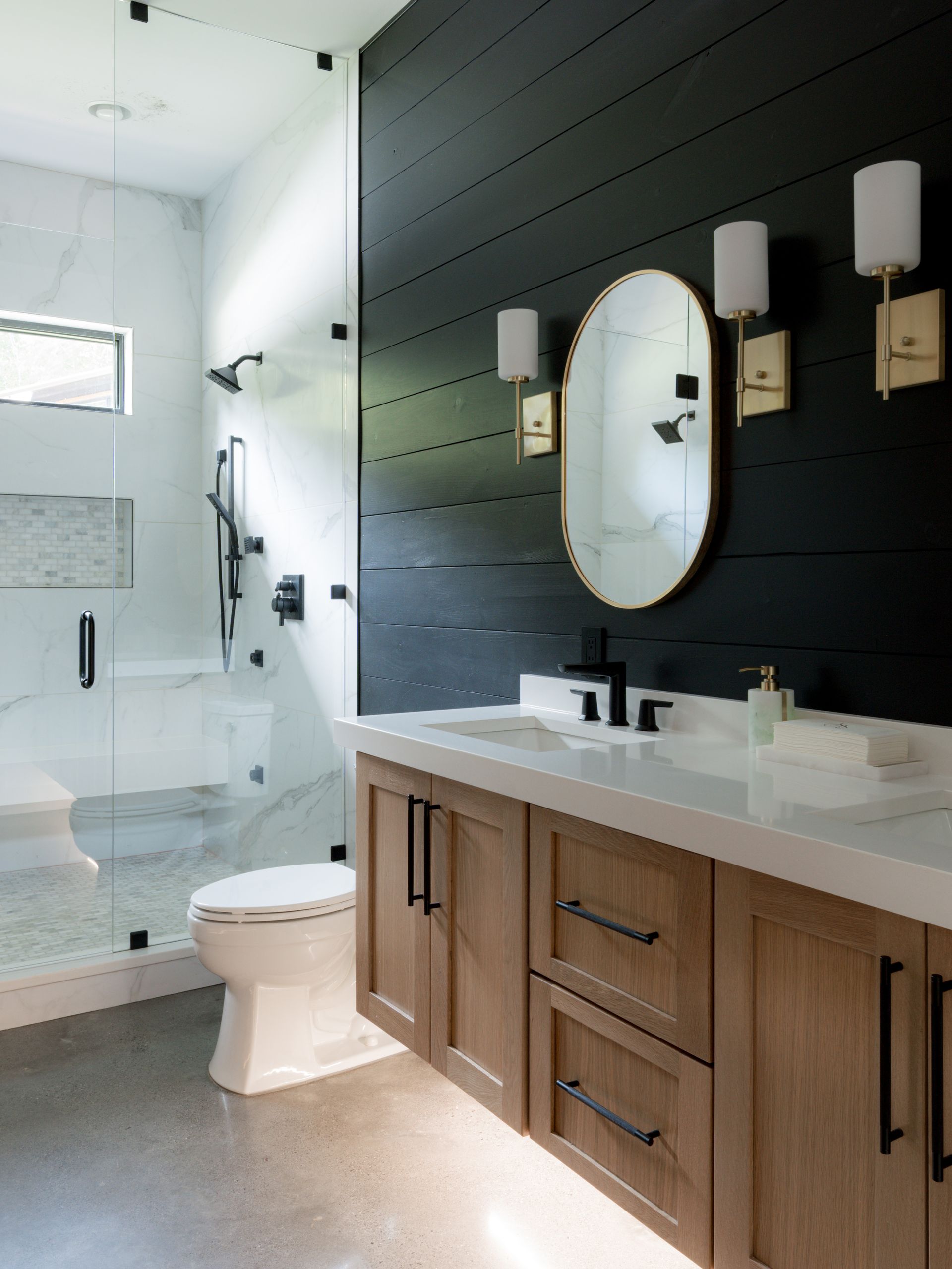 Modern bathroom with glass shower, black accent wall, wood vanity, and white toilet