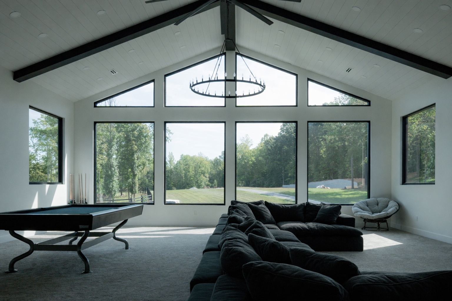 Modern living room with floor-to-ceiling windows, black sectional sofa, chaise lounge, and chandelier.