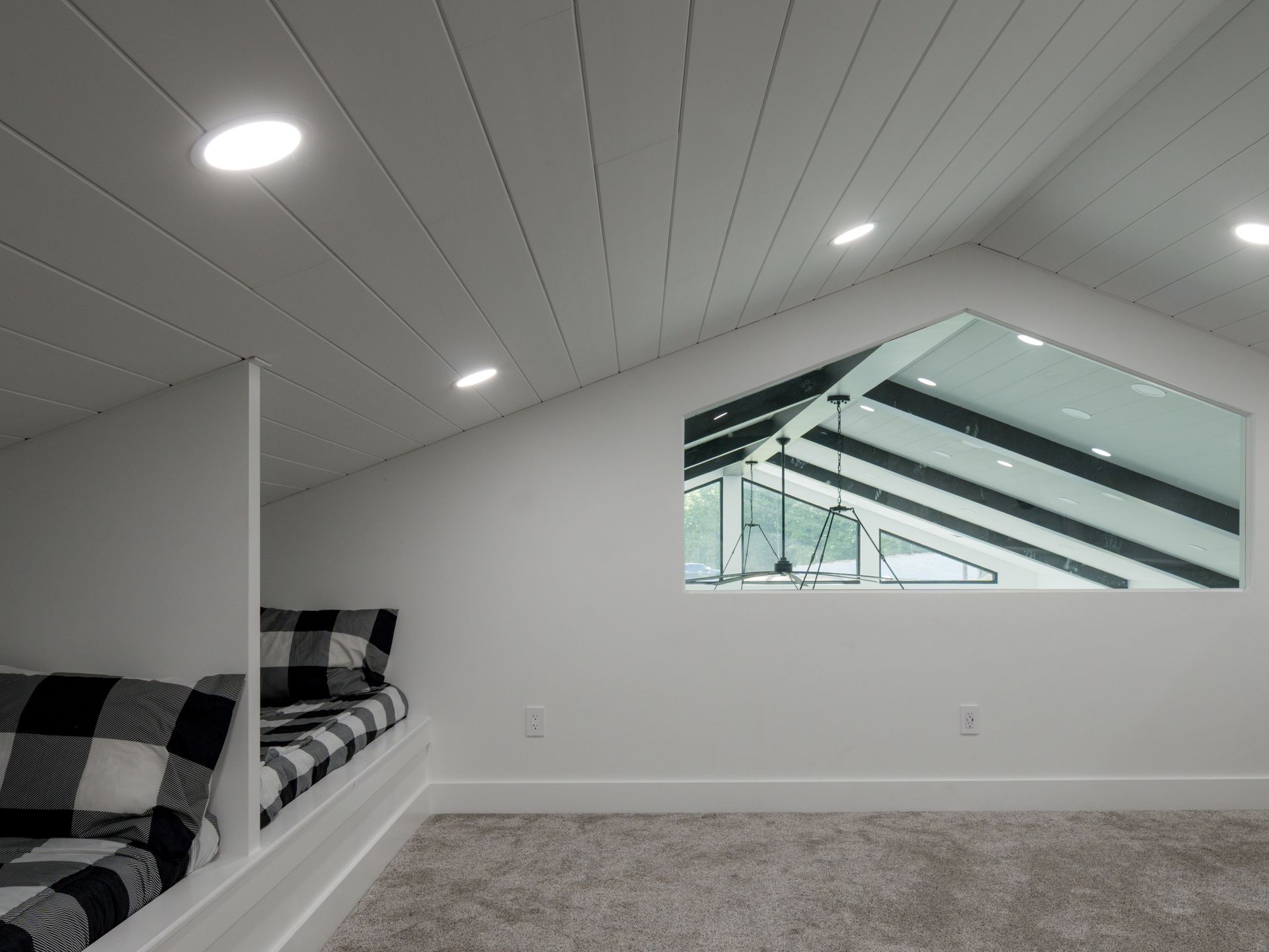 Bright loft bedroom with sloped white ceiling, recessed lights, bed, and a large mirror reflecting stairs.
