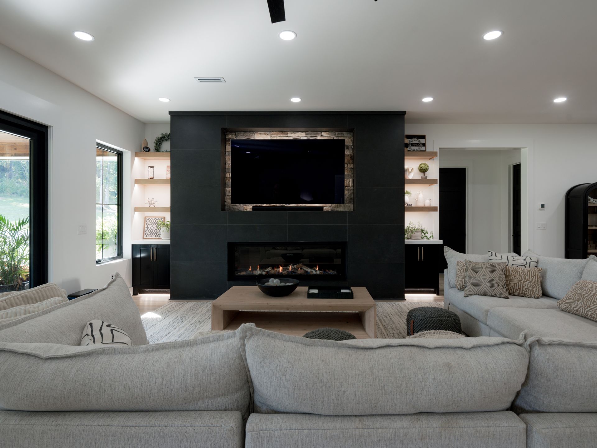 Bright modern living room with gray sofas, black fireplace wall, wall-mounted TV, and recessed lighting