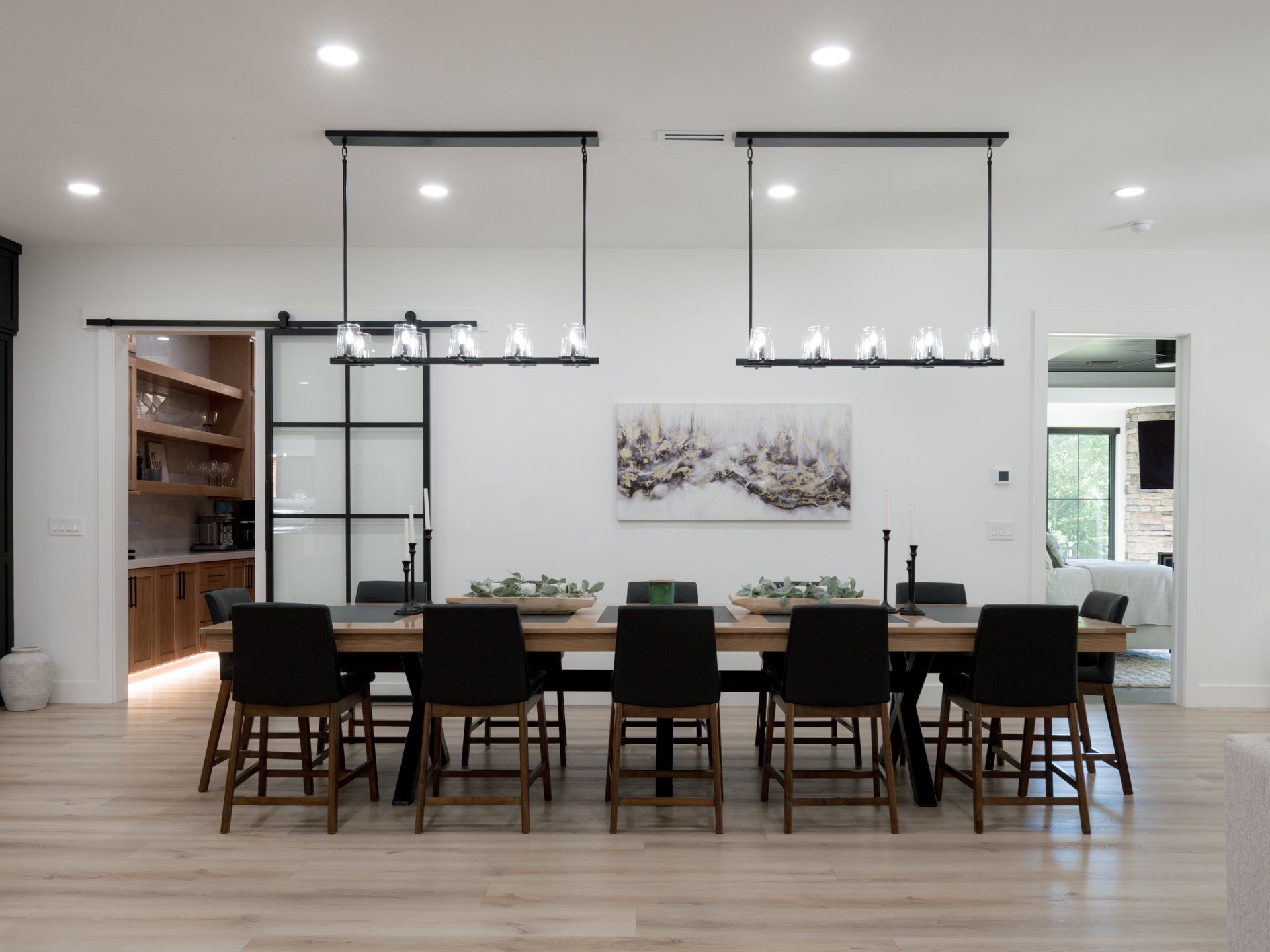 Modern dining room with long black table, eight chairs, pendant lights, and white walls